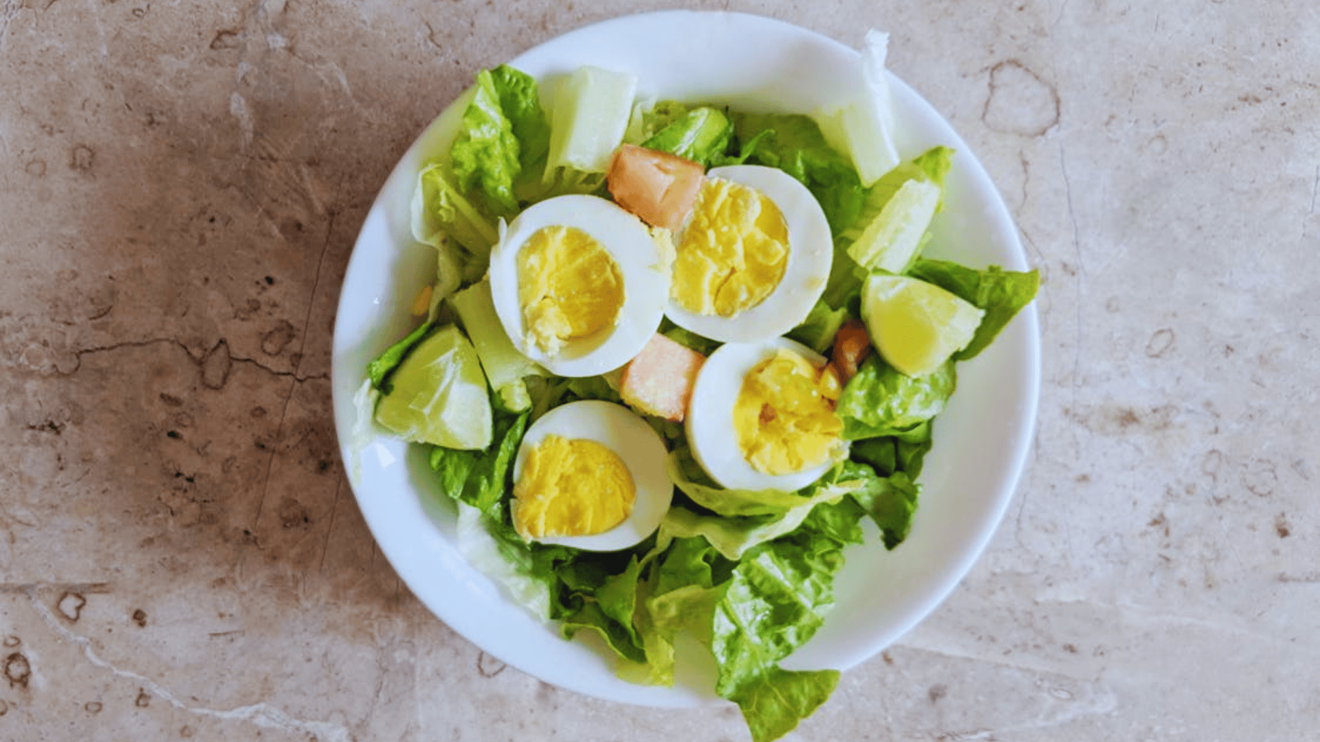 hard boiled egg salad with lettuce cucumber and lime in a white bowl