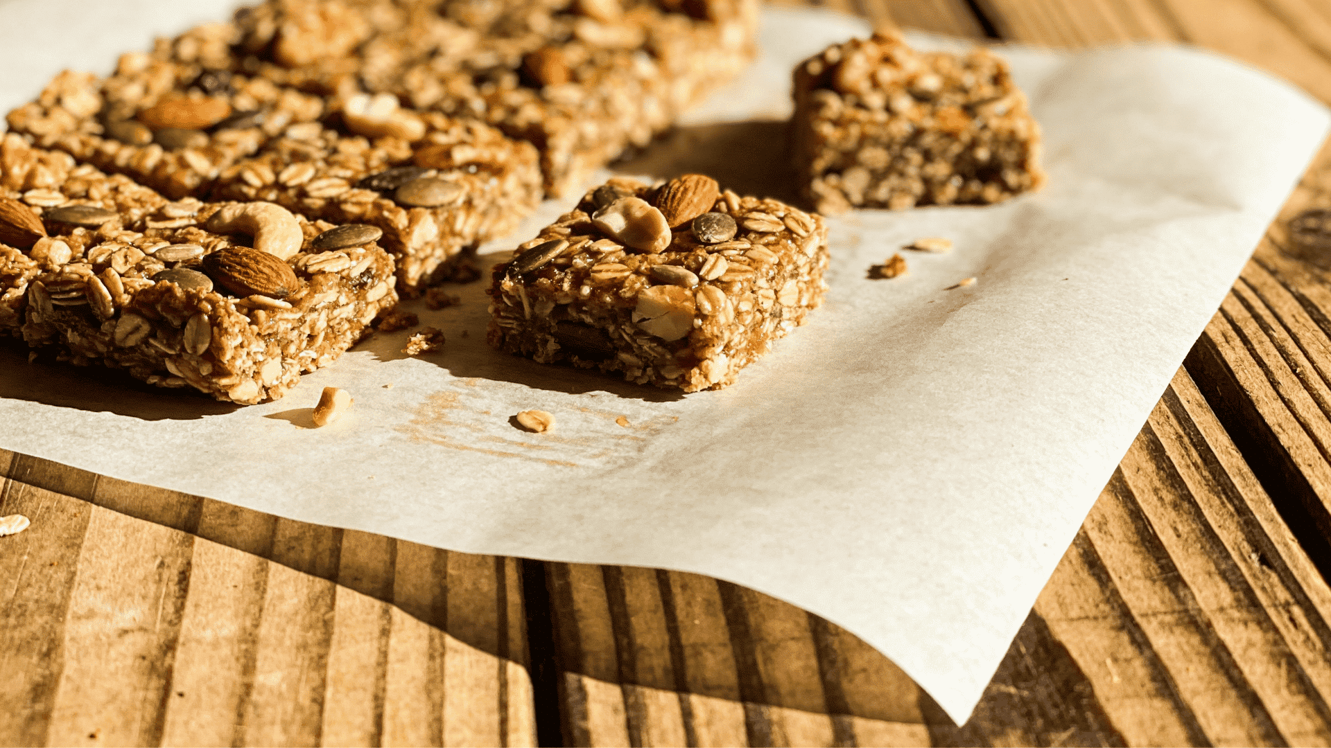 homemade granola bars with oats nuts and seeds on parchment paper on wooden table in warm natural light