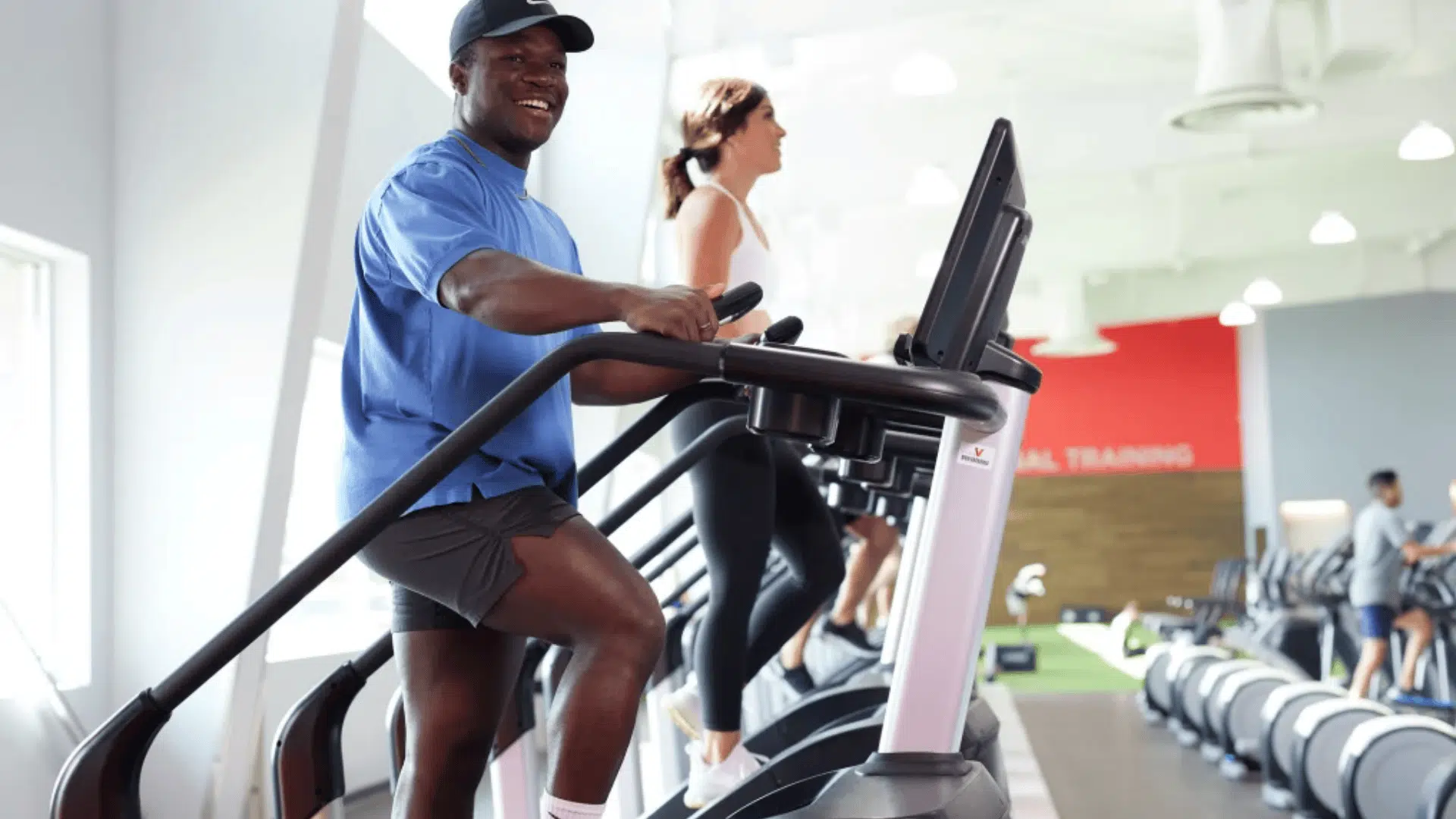man using stair climber machine at gym doing cardio workout while another person exercises in background