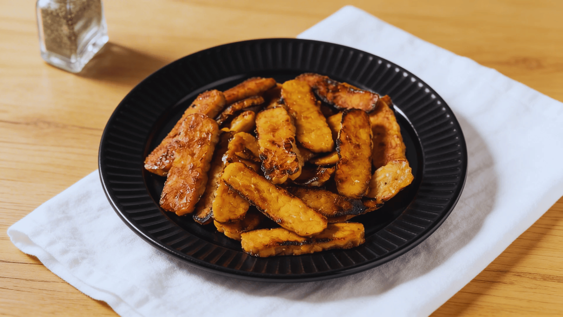 pan fried tempeh strips on black plate with seasoning