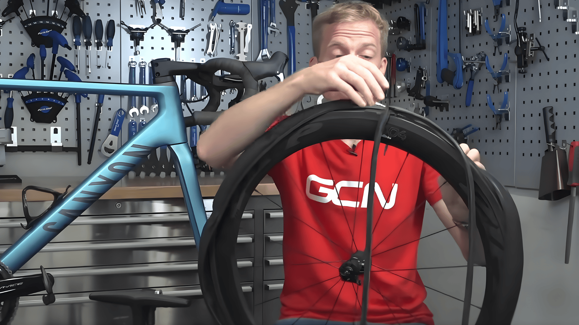 person removing inner tube from bike wheel in workshop demonstrating how to change bike tire with tools and road bike visible