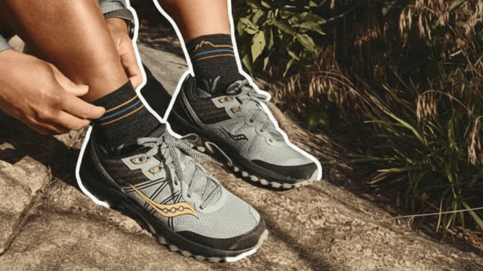 person sitting on rock adjusting sock wearing gray running shoes and black socks in sunny outdoor natural setting