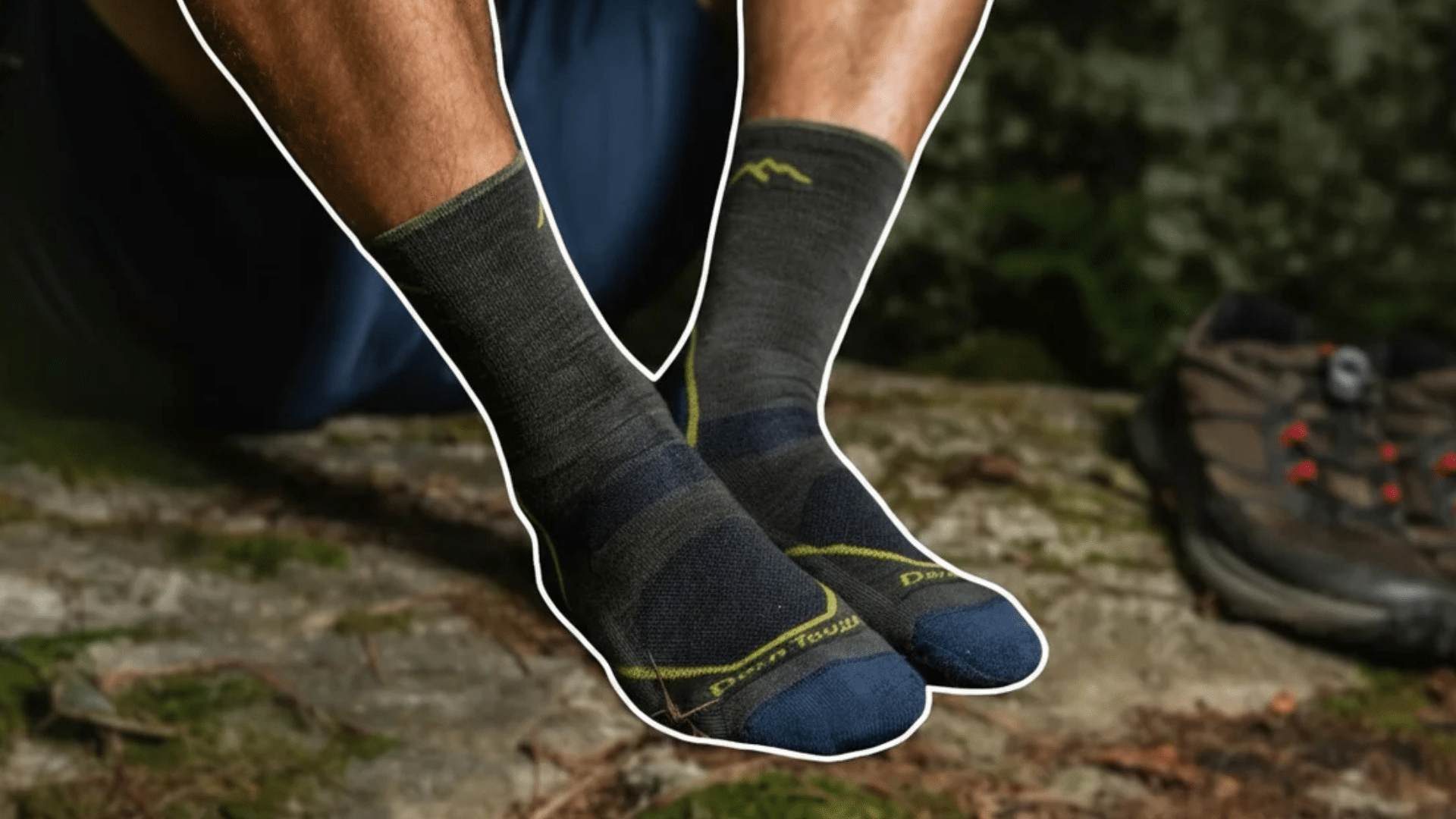 person sitting on rock wearing dark socks with hiking boots nearby in forest outdoor setting