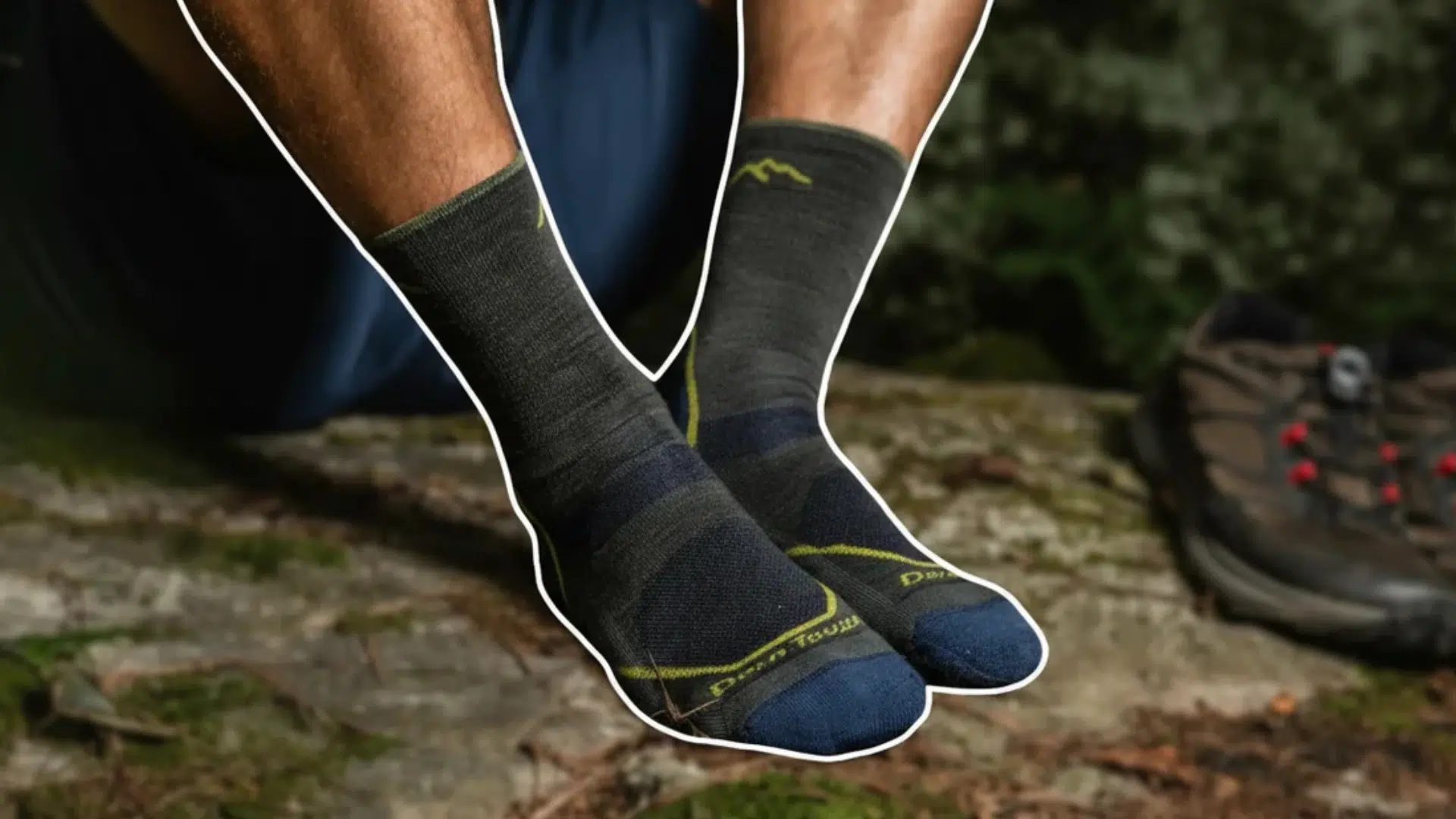 person sitting on rock wearing dark socks with hiking boots nearby in forest outdoor setting