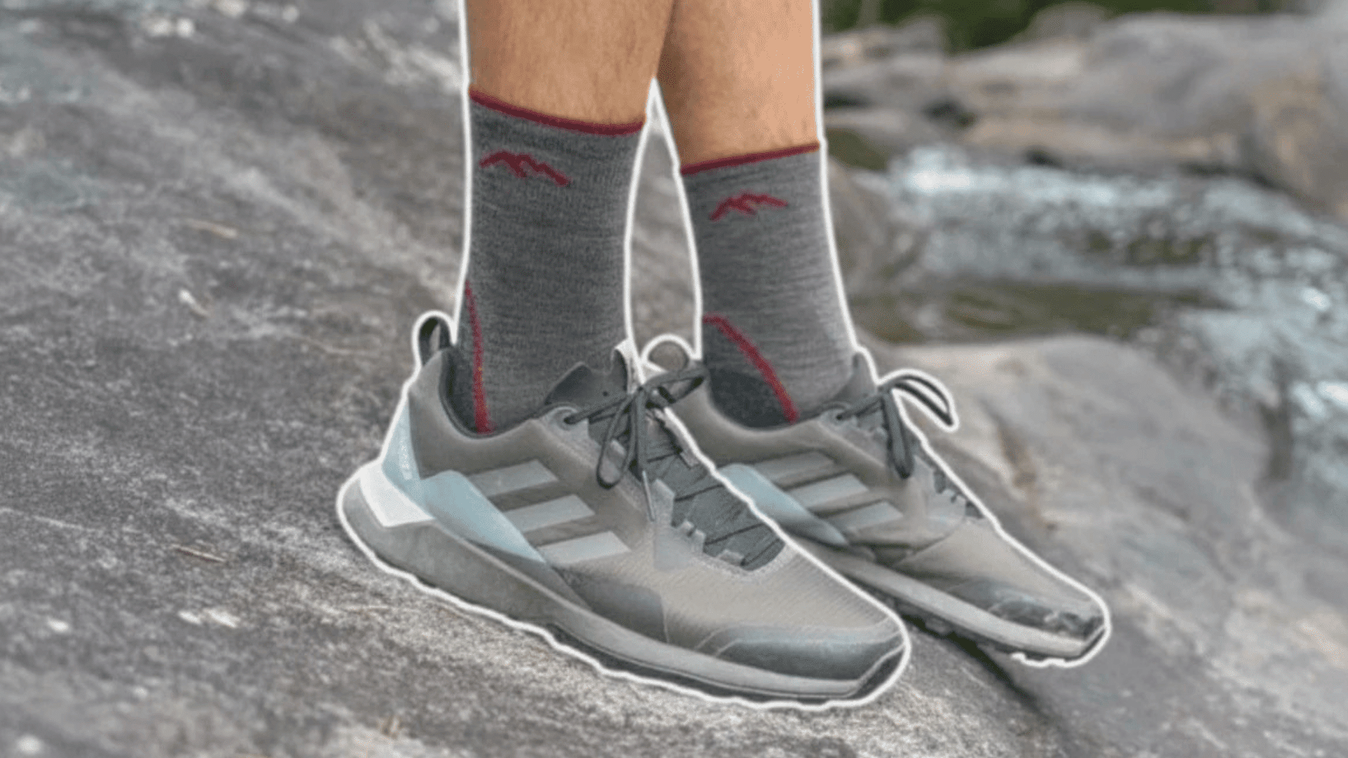 person standing on rock near water wearing gray shoes and gray socks with red detail in outdoor natural setting