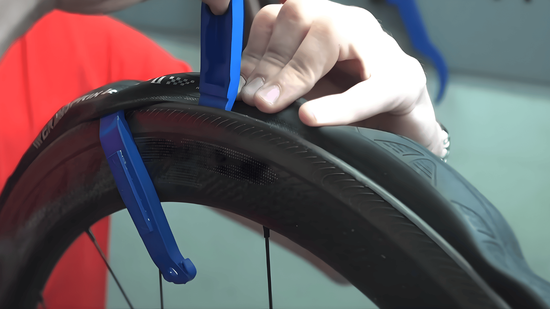 person using blue tire levers to remove bike tire from rim demonstrating how to change bike tire close up hands and wheel