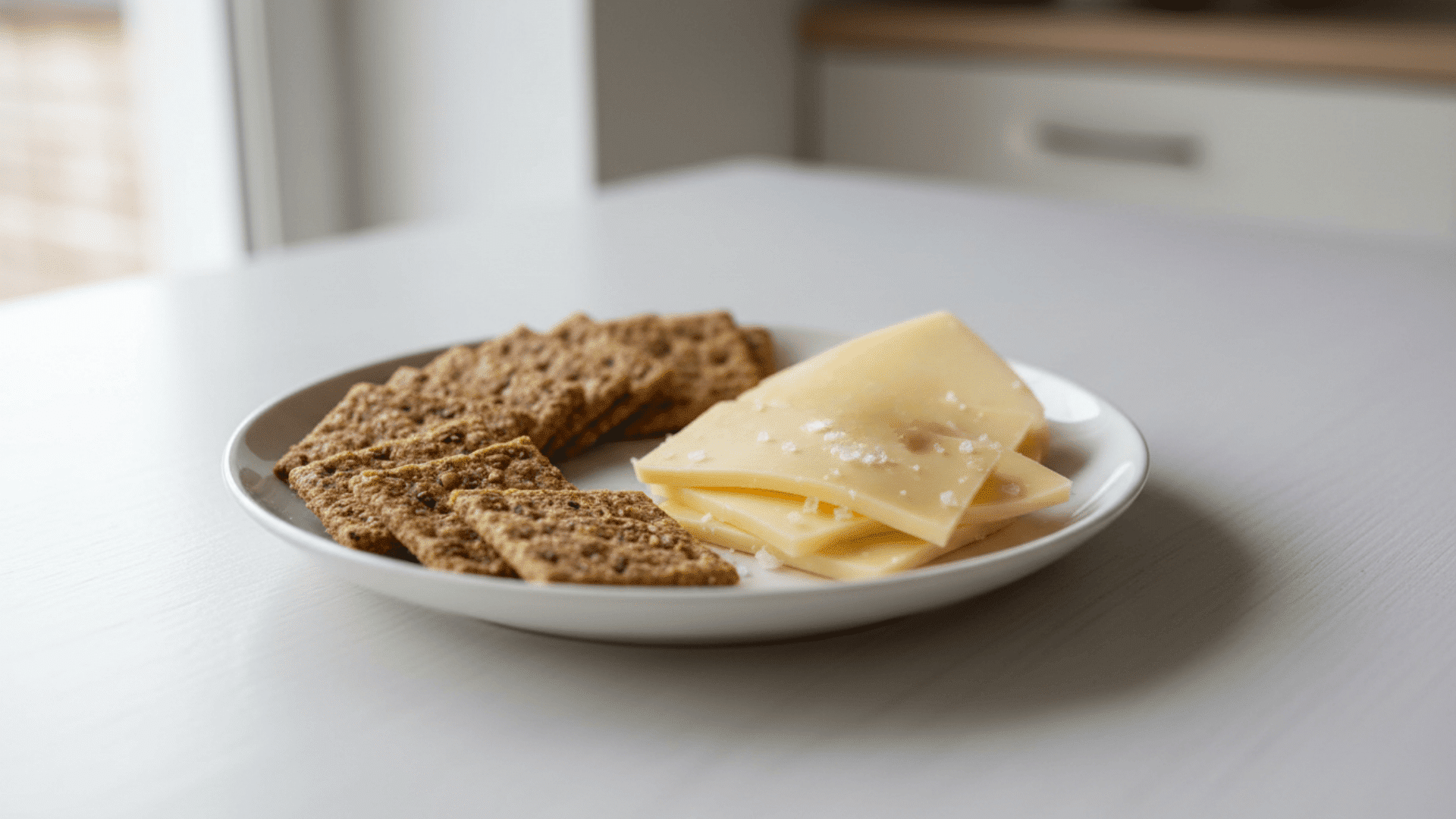 plate with seeded crackers and slices of cheese sprinkled with salt on table in soft natural light