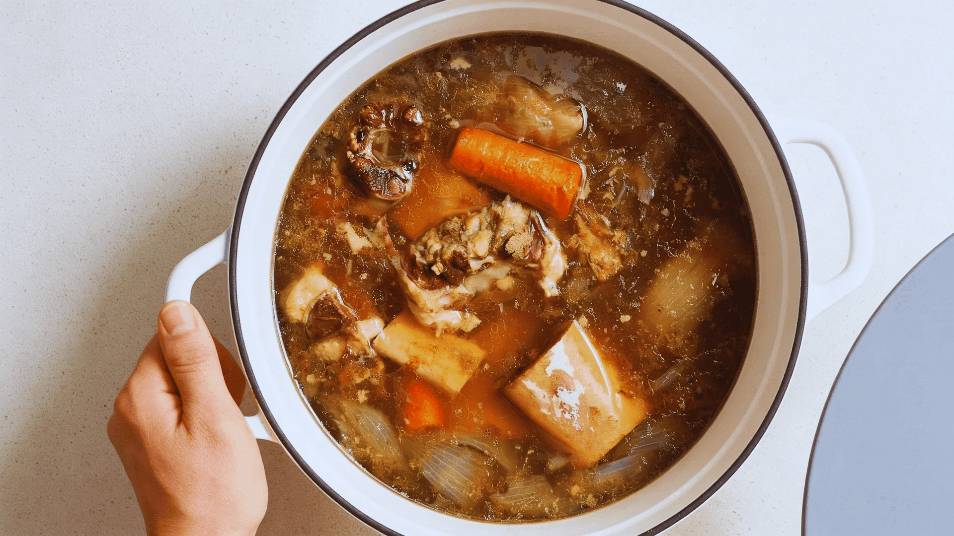 pot of homemade bone broth with carrots onions and meat simmering