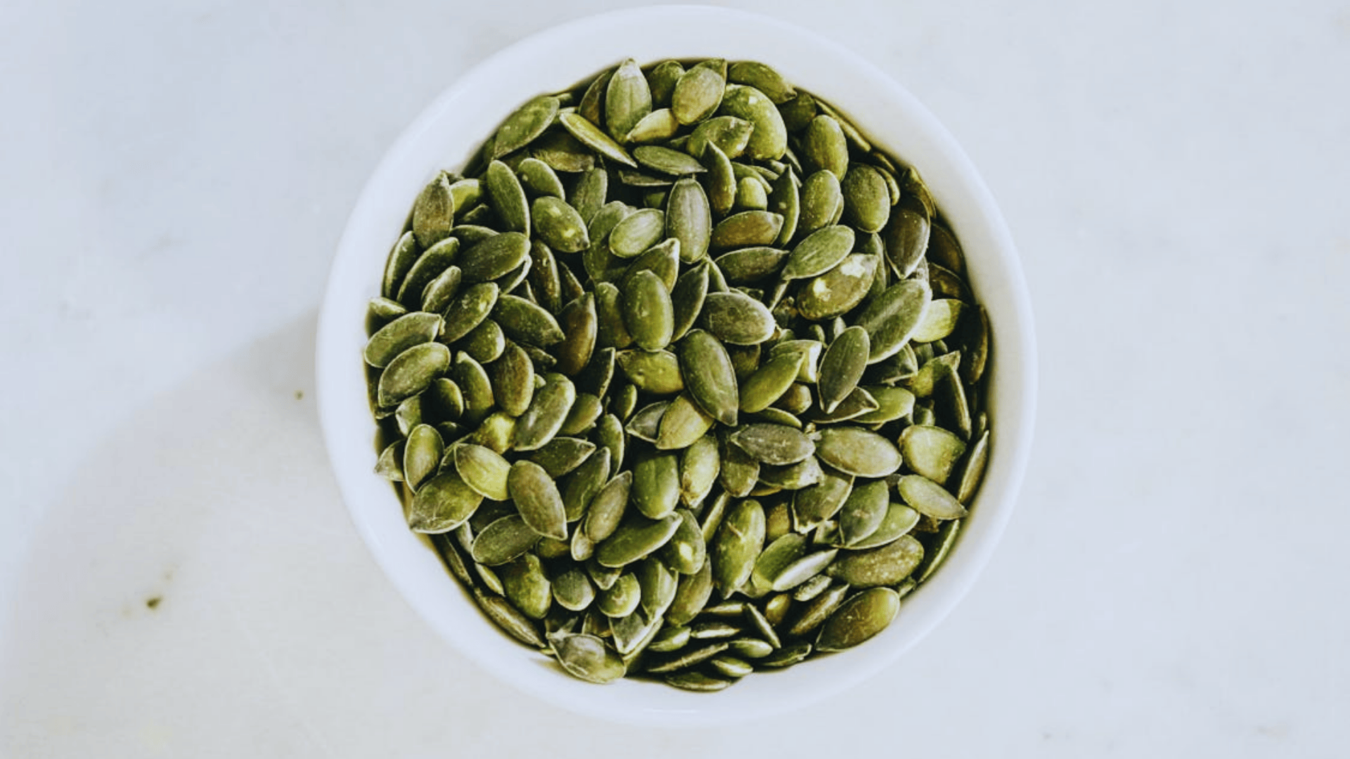 pumpkin seeds in a white bowl on a light background