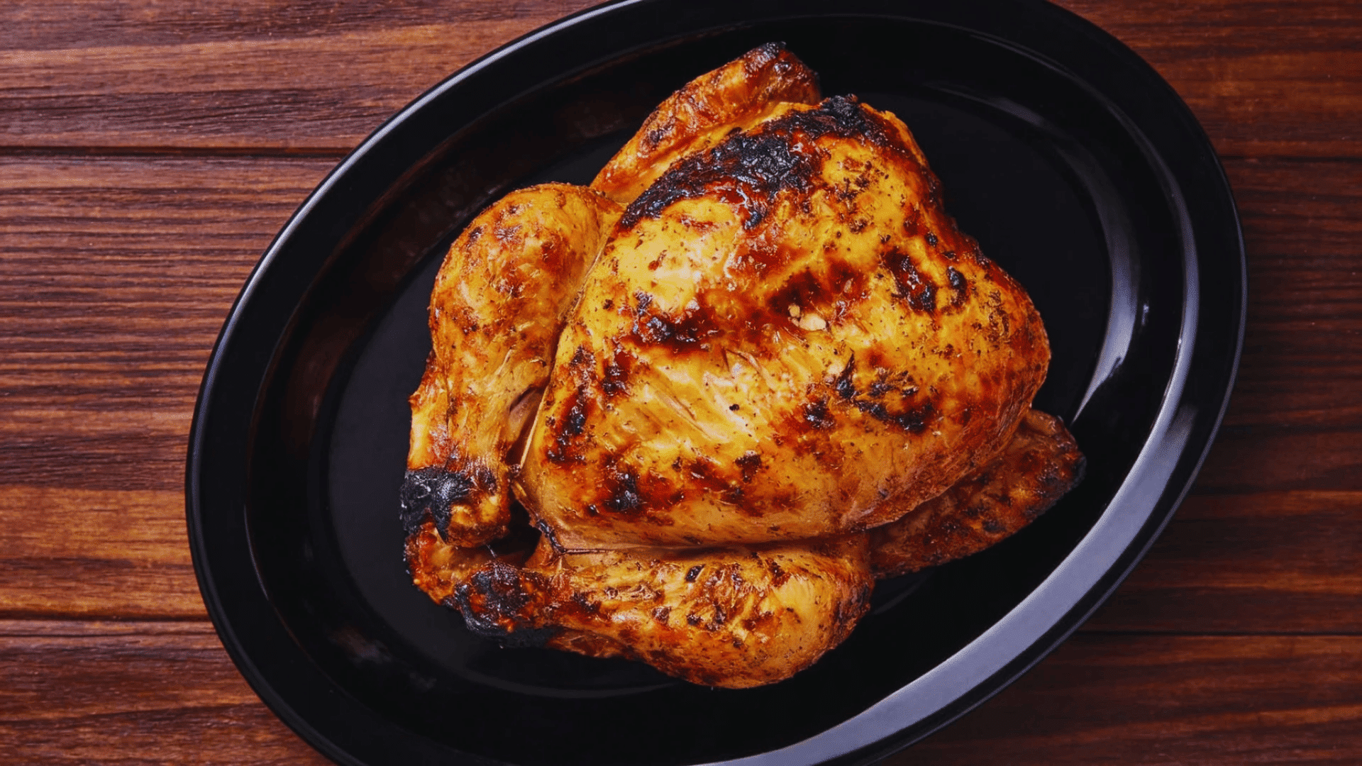 roasted whole chicken on a black plate on a wooden table