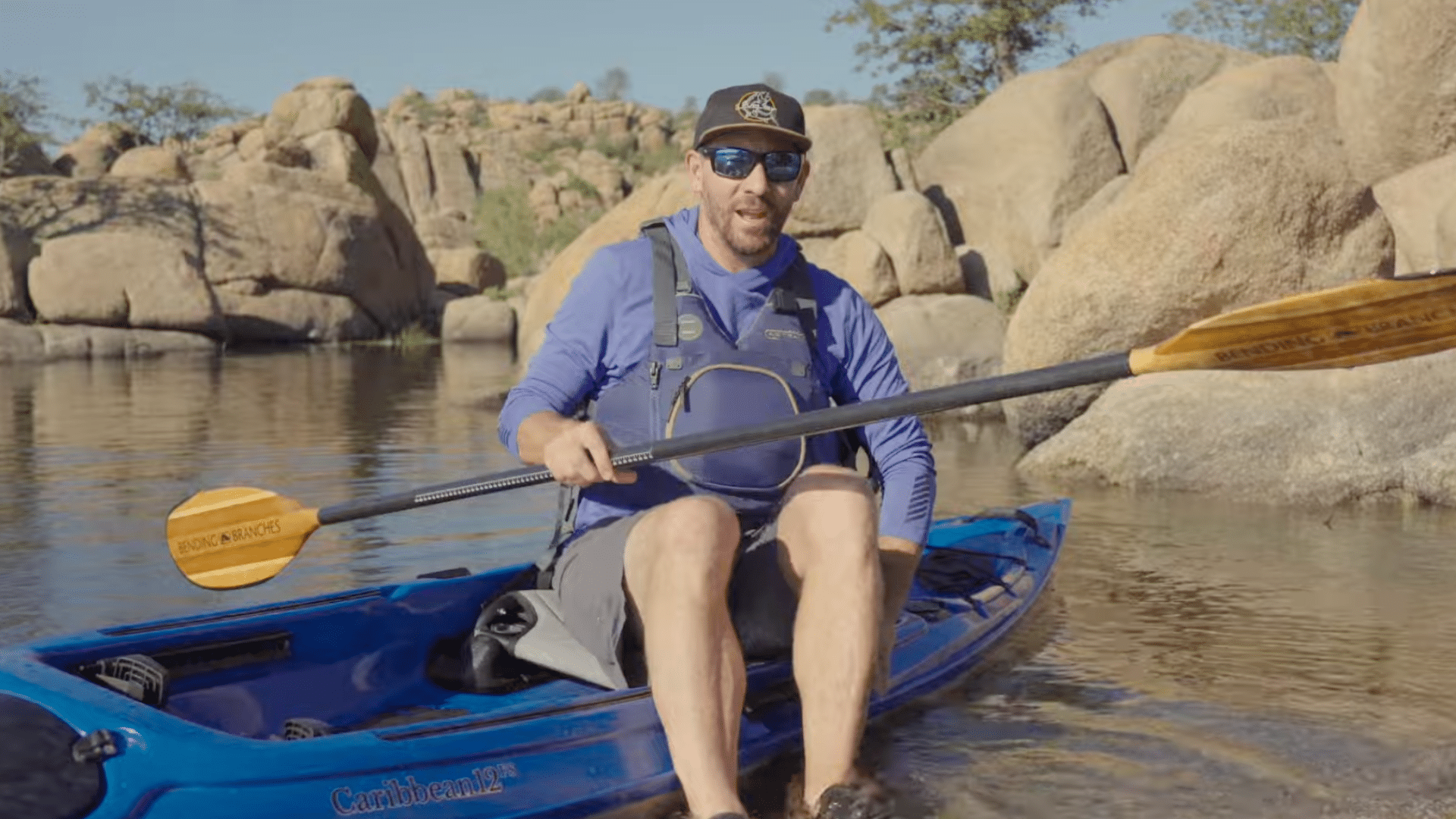 steps out of a kayak in shallow water holding the sides for balance while exiting carefully to avoid tipping over
