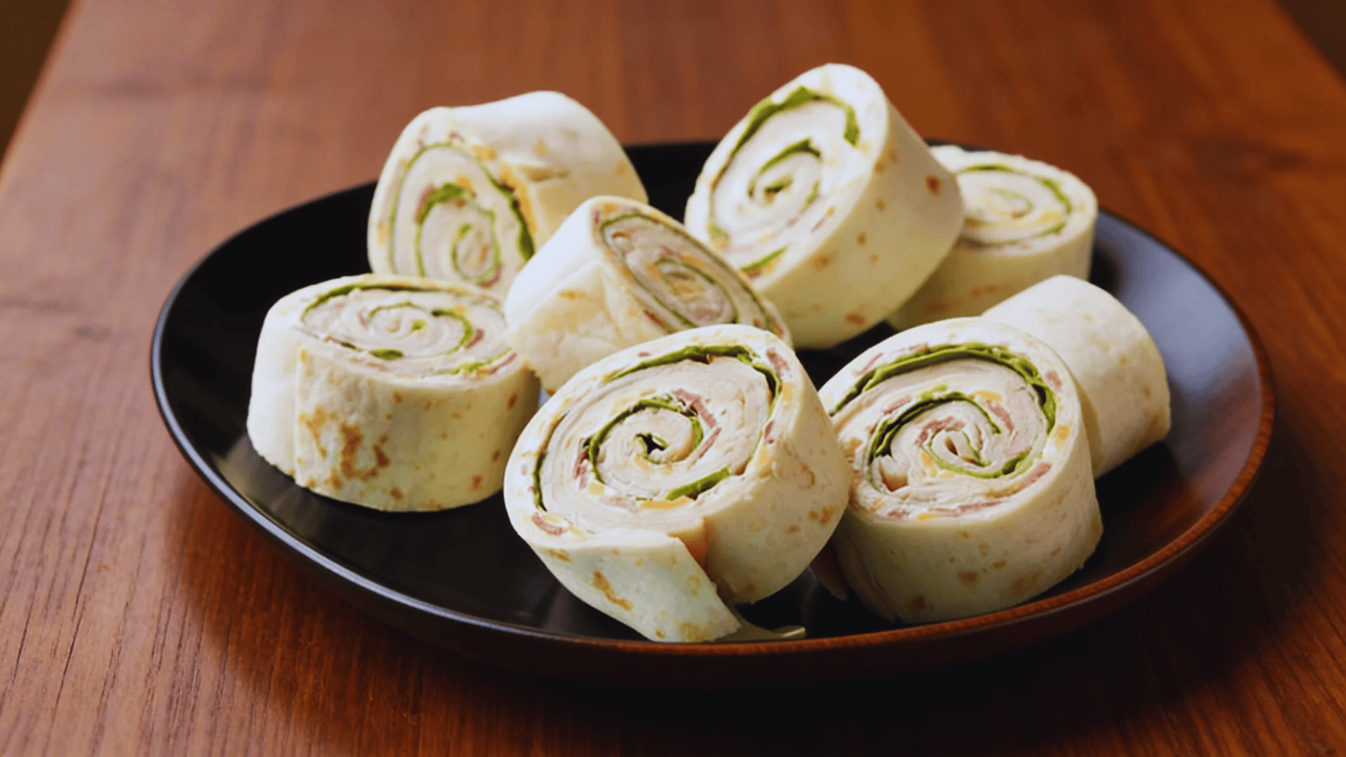 turkey roll ups with tortilla and greens on a black plate