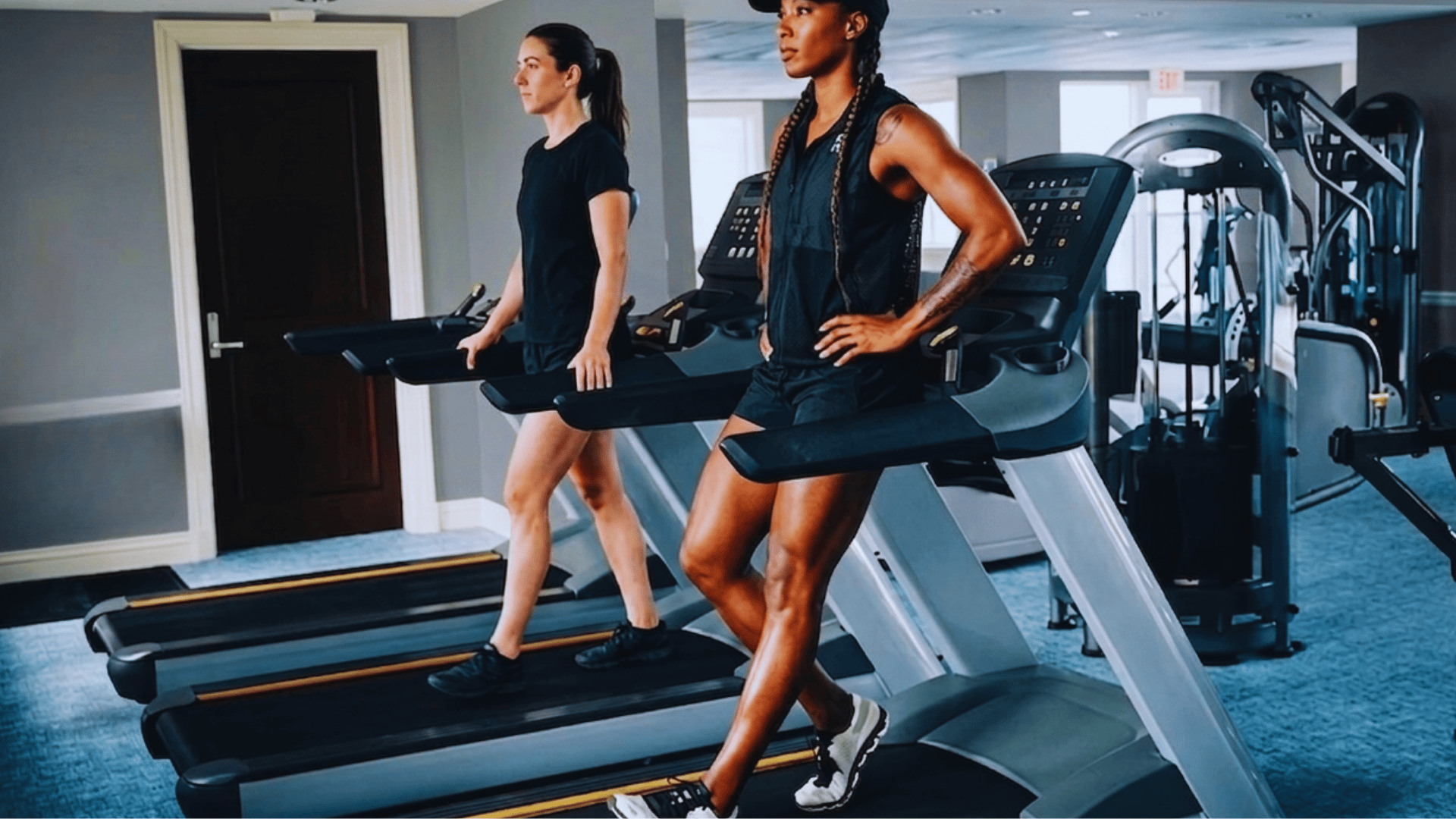 two women walking backward on treadmills in a gym during workout