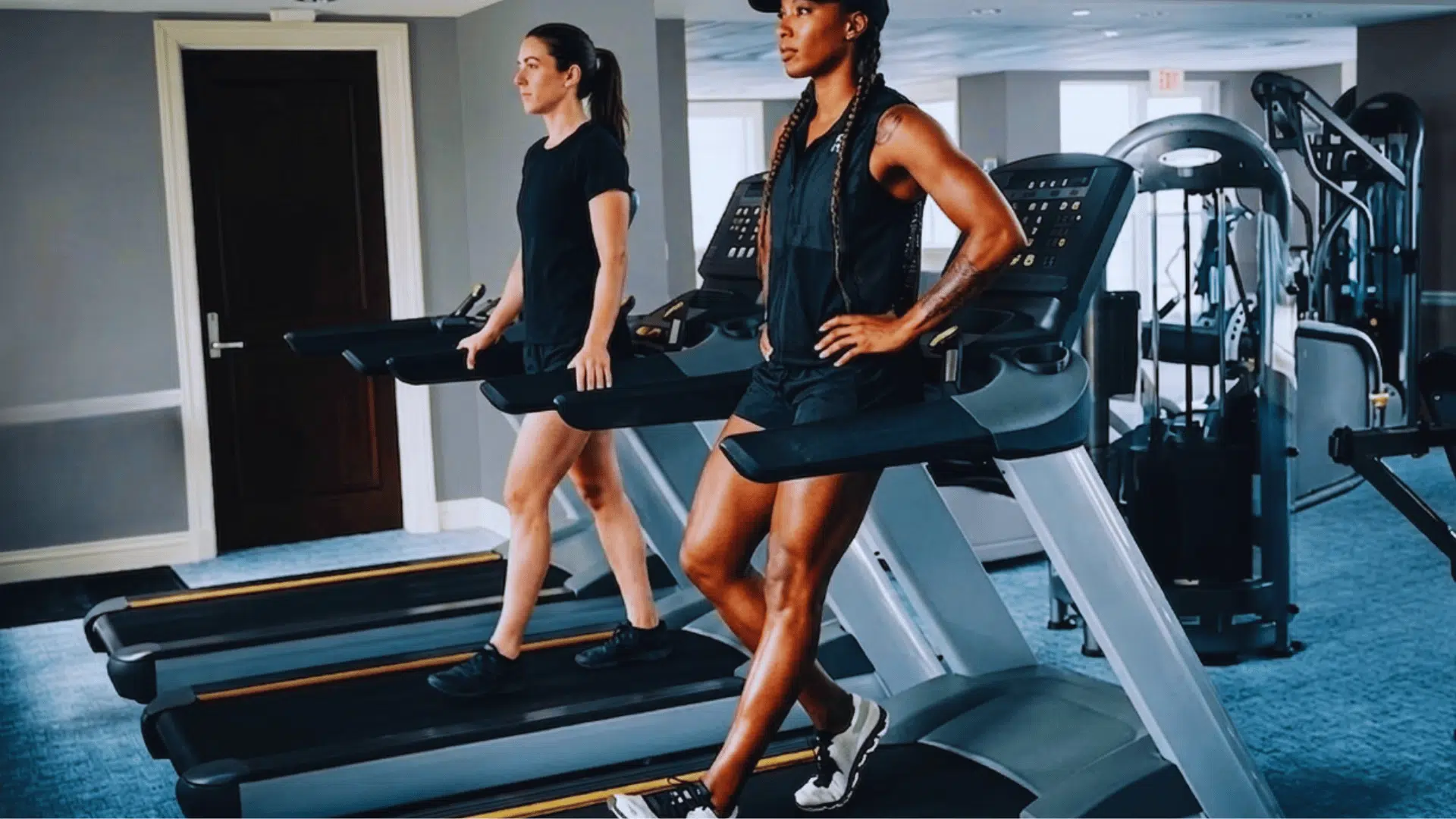 two women walking backward on treadmills in a gym during workout