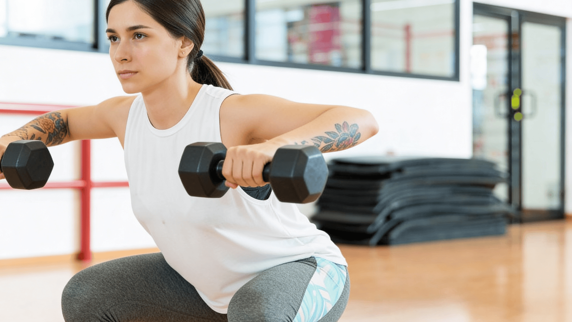 woman performing squat with dumbbells in gym wearing white top focusing on strength training and upper body exercise