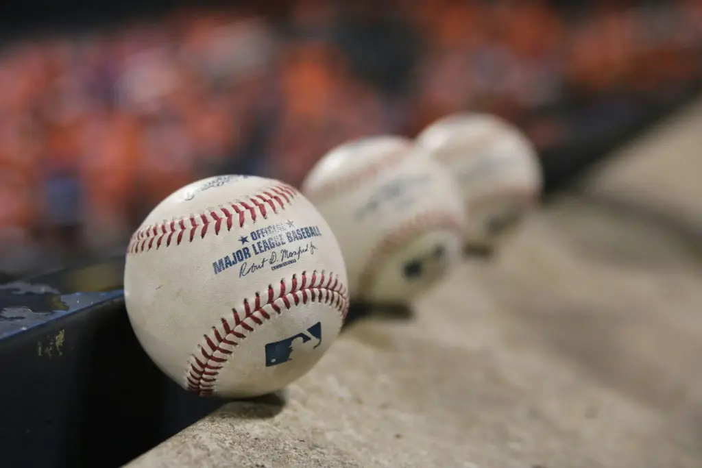 Major League baseballs lined up on a concrete ledge with blurred stadium background
