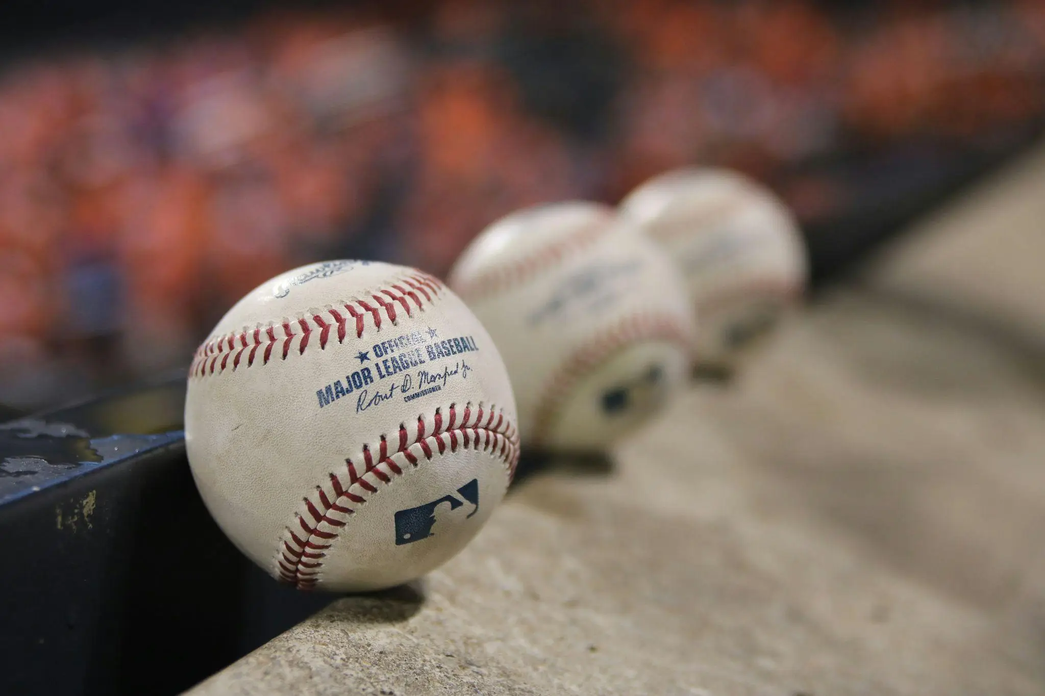 Major League baseballs lined up on a concrete ledge with blurred stadium background