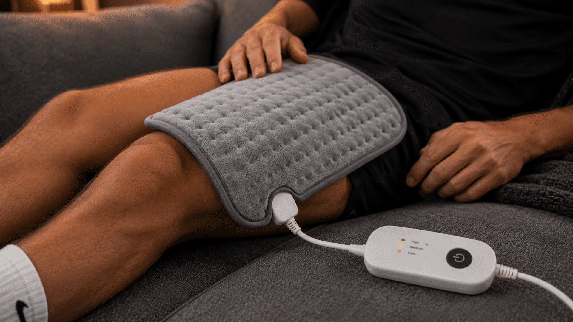 athlete relaxing with a heating pad on leg muscles during a recovery session on a living room couch