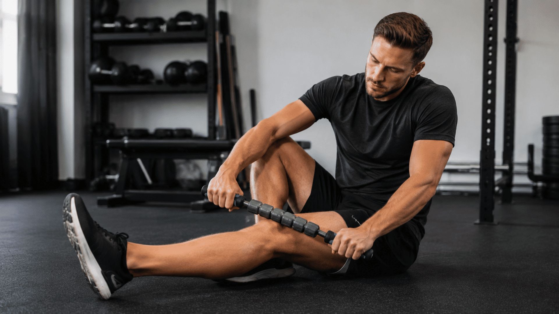 athlete using a massage stick on leg muscles during a recovery session in a modern gym setting