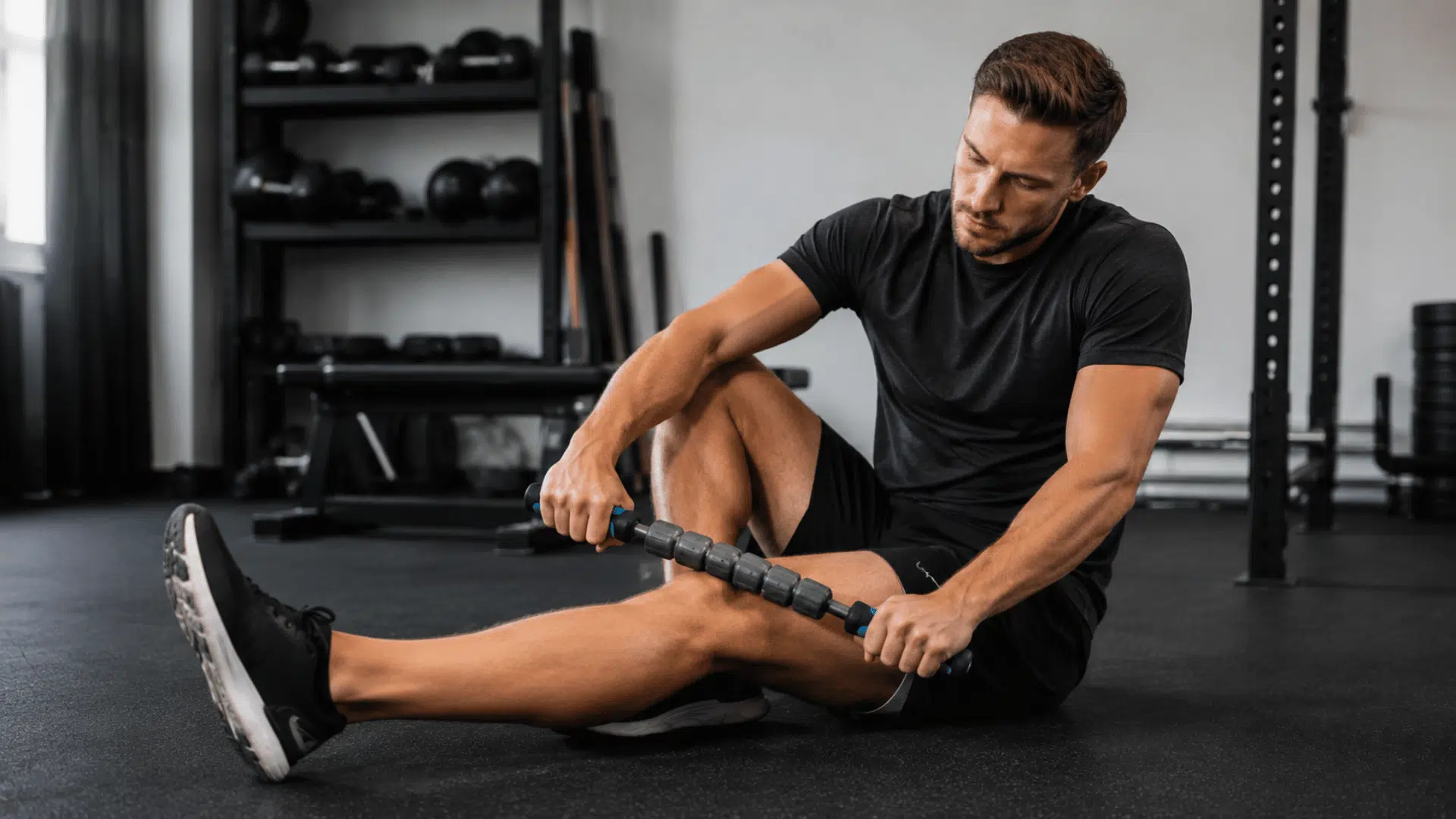 athlete using a massage stick on leg muscles during a recovery session in a modern gym setting