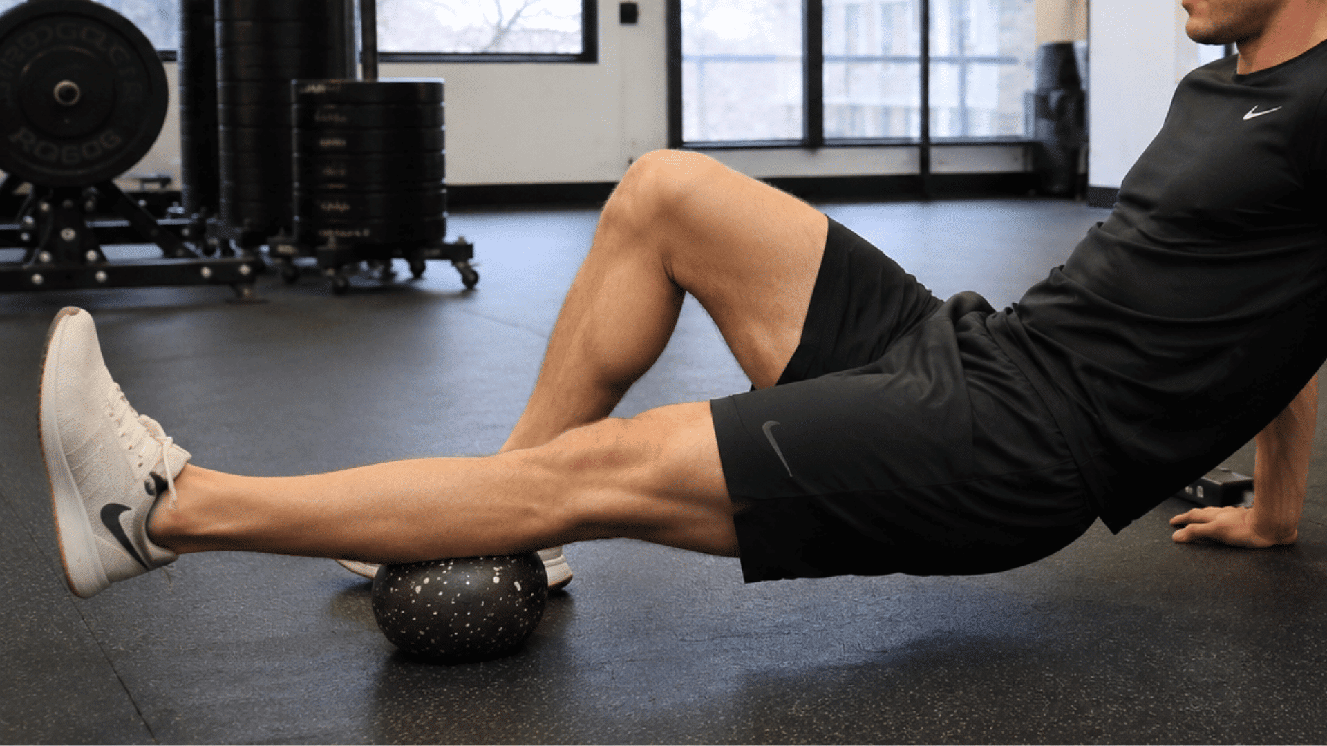 athlete using a mobility ball for leg muscle recovery and stretching during a gym workout session