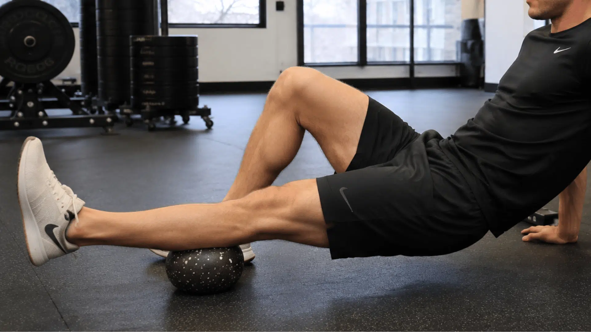 athlete using a mobility ball for leg muscle recovery and stretching during a gym workout session