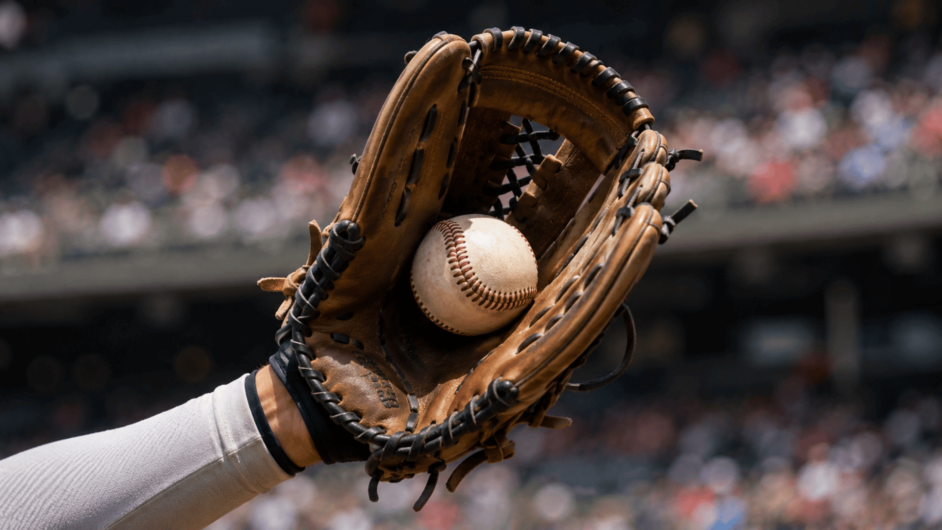baseball glove catching ball during fast paced game with blurred stadium crowd in background