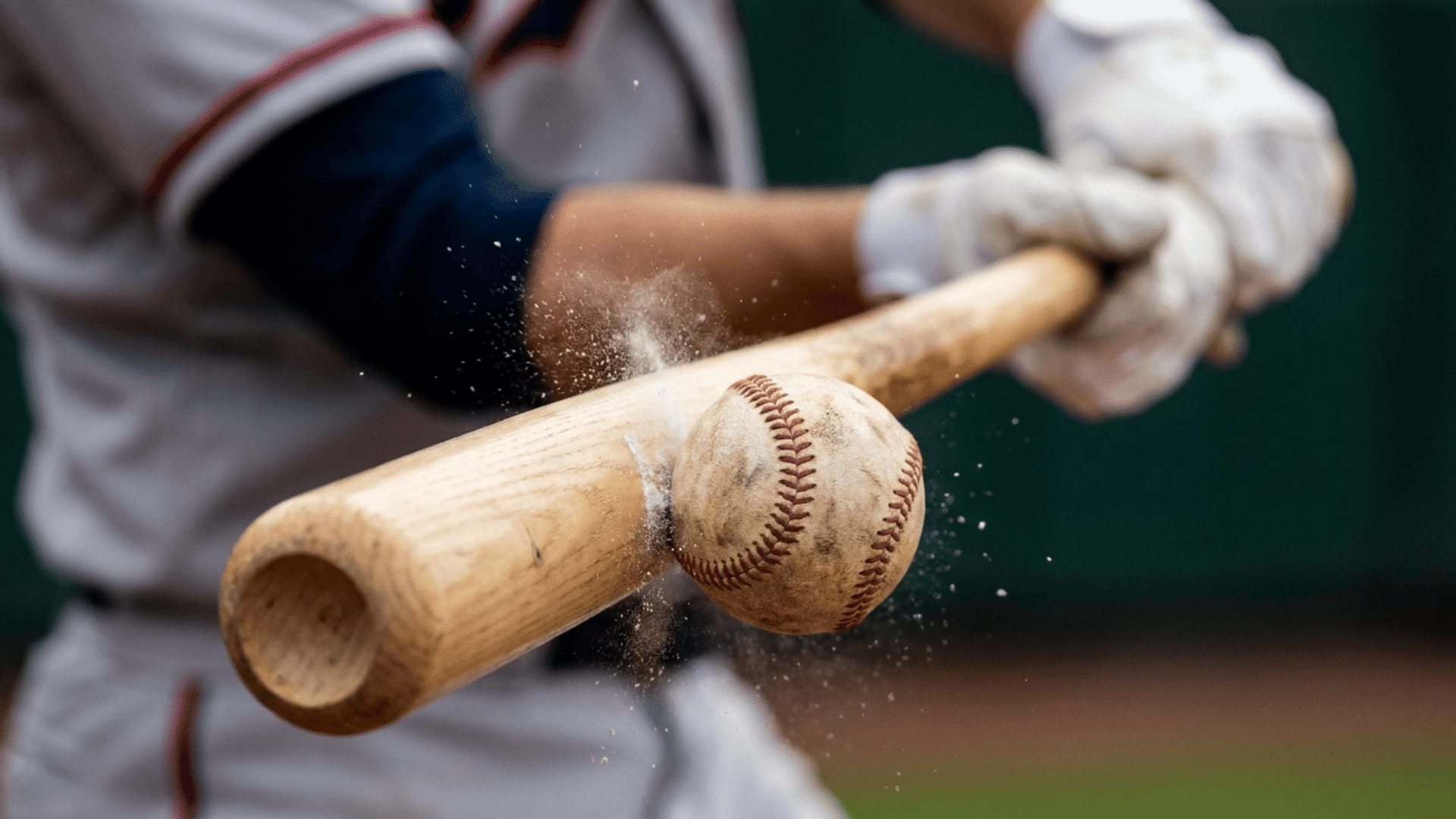 close view of baseball hitting wooden bat during live game with player swinging in the background