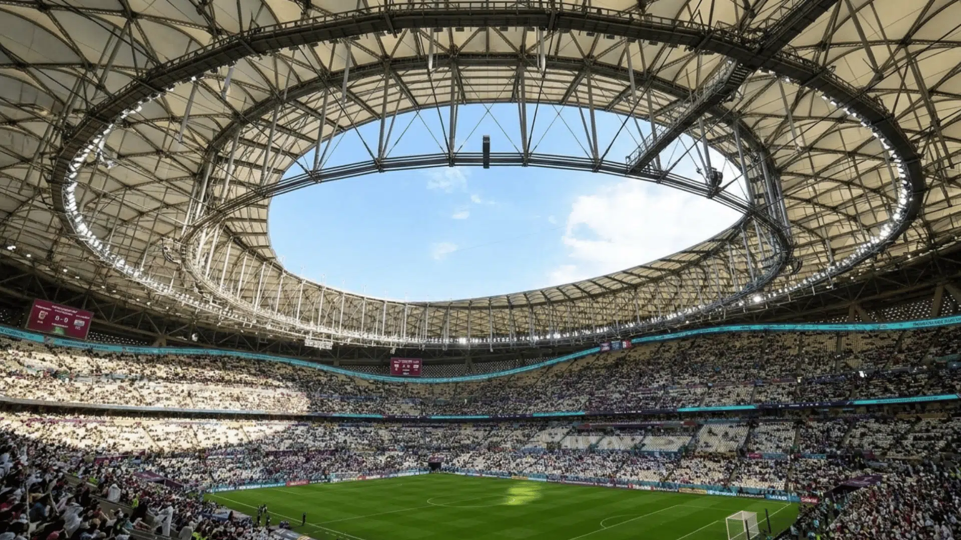 crowded football stadium beneath a curved roof with sunlight shining over the green field and fans
