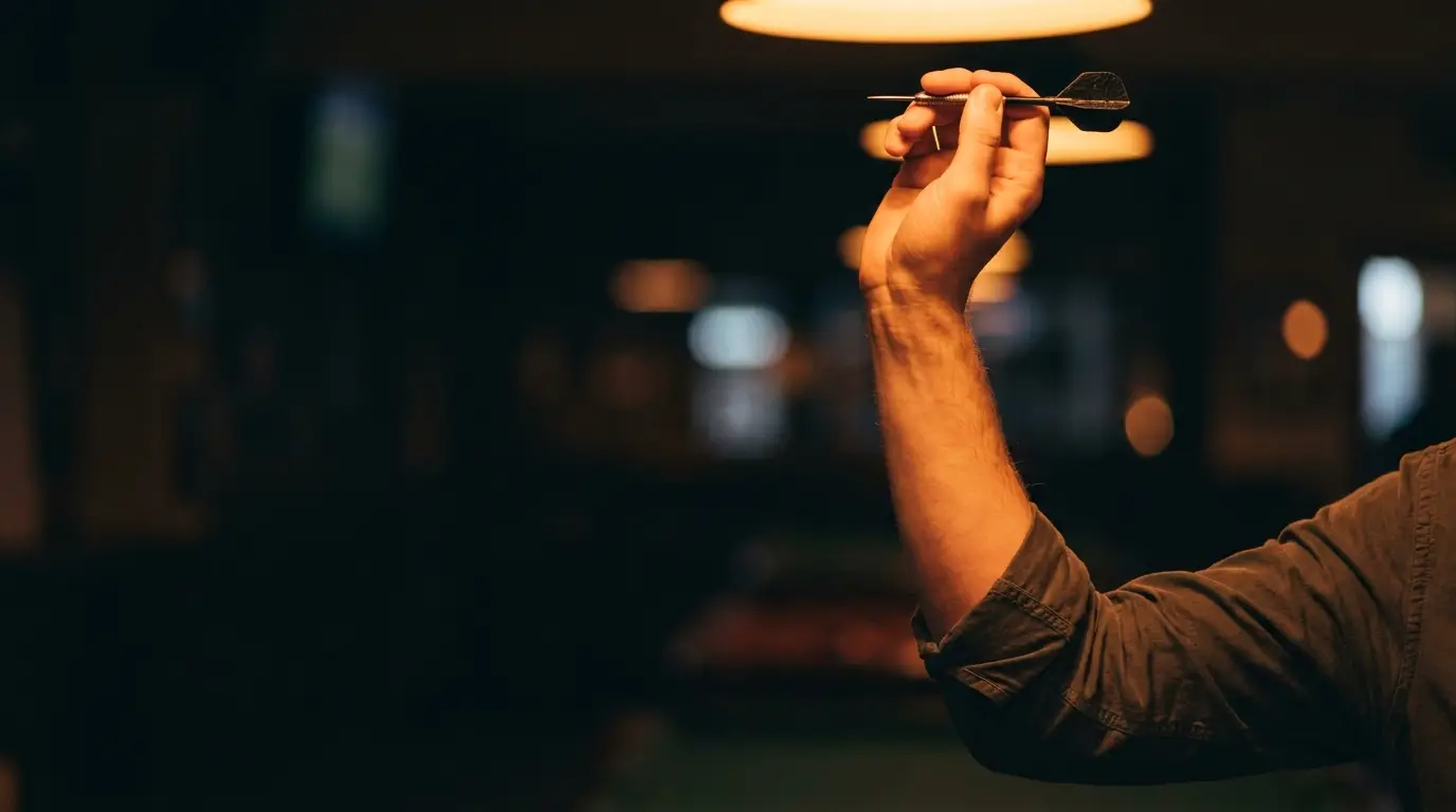 Hand aiming a dart in dimly lit bar setting