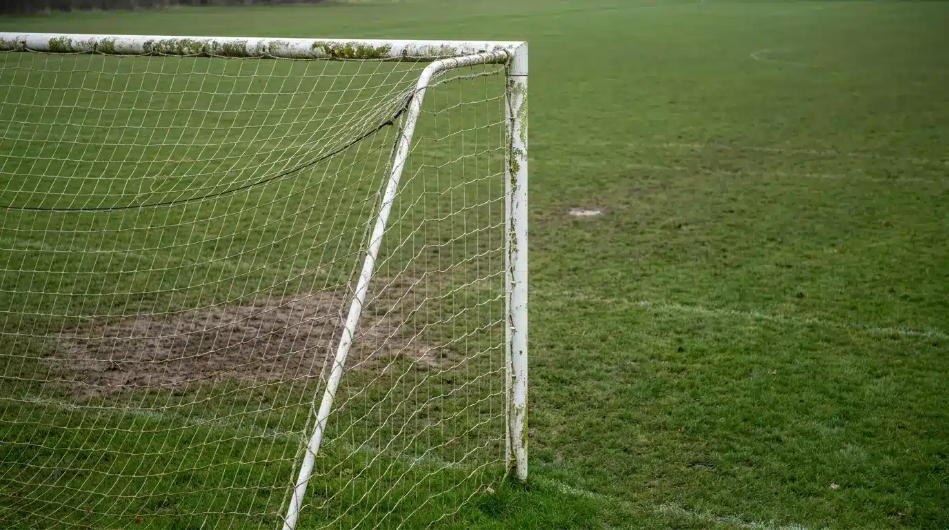 Rustic soccer goal on a grassy field with worn patches under overcast sky