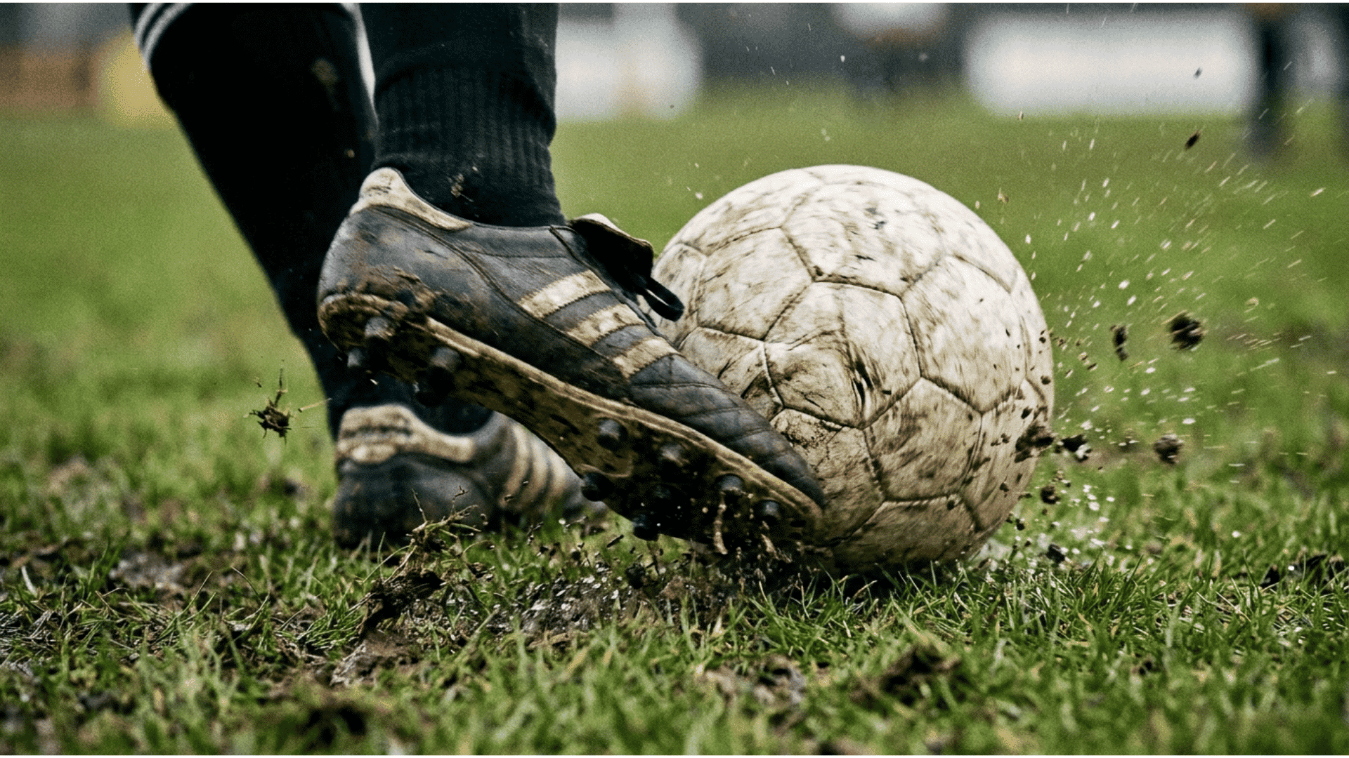 soccer player kicking a muddy ball on wet grass during an outdoor match with dirt flying through the air