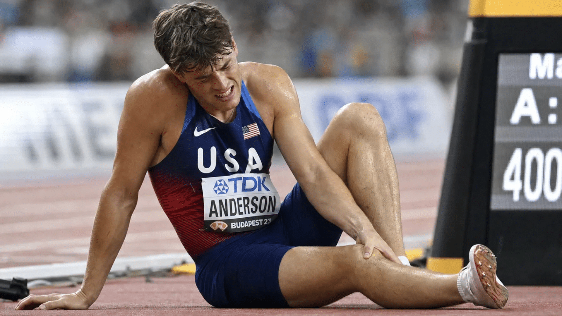 track athlete sitting on the ground holding his leg in pain after a race during a stadium competition