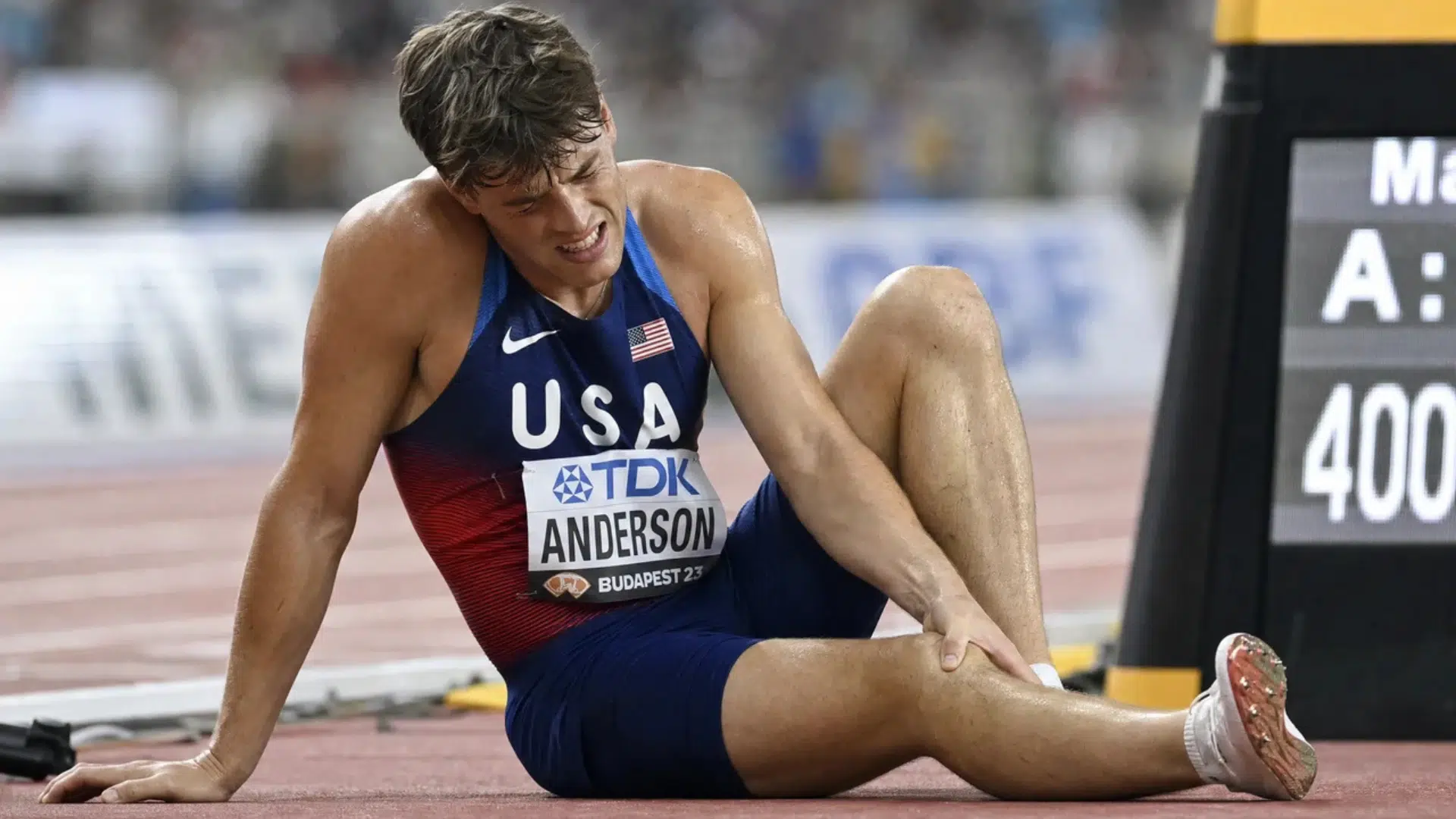 track athlete sitting on the ground holding his leg in pain after a race during a stadium competition