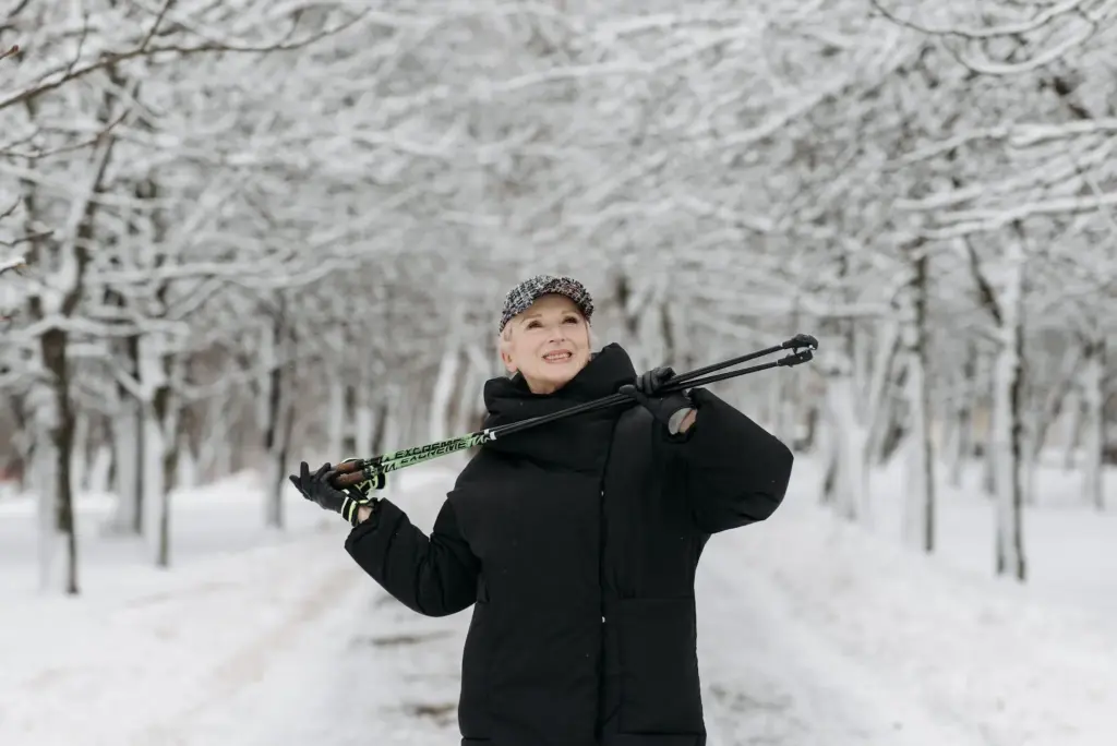 Person in black winter coat holding trekking poles in snowy tree-lined path