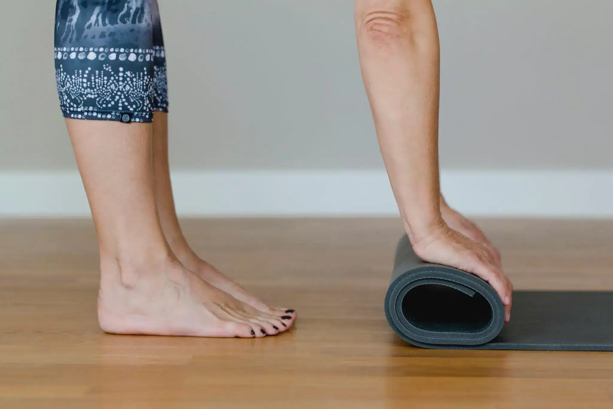 Bare feet on wooden floor as yoga mat is rolled up in bright room