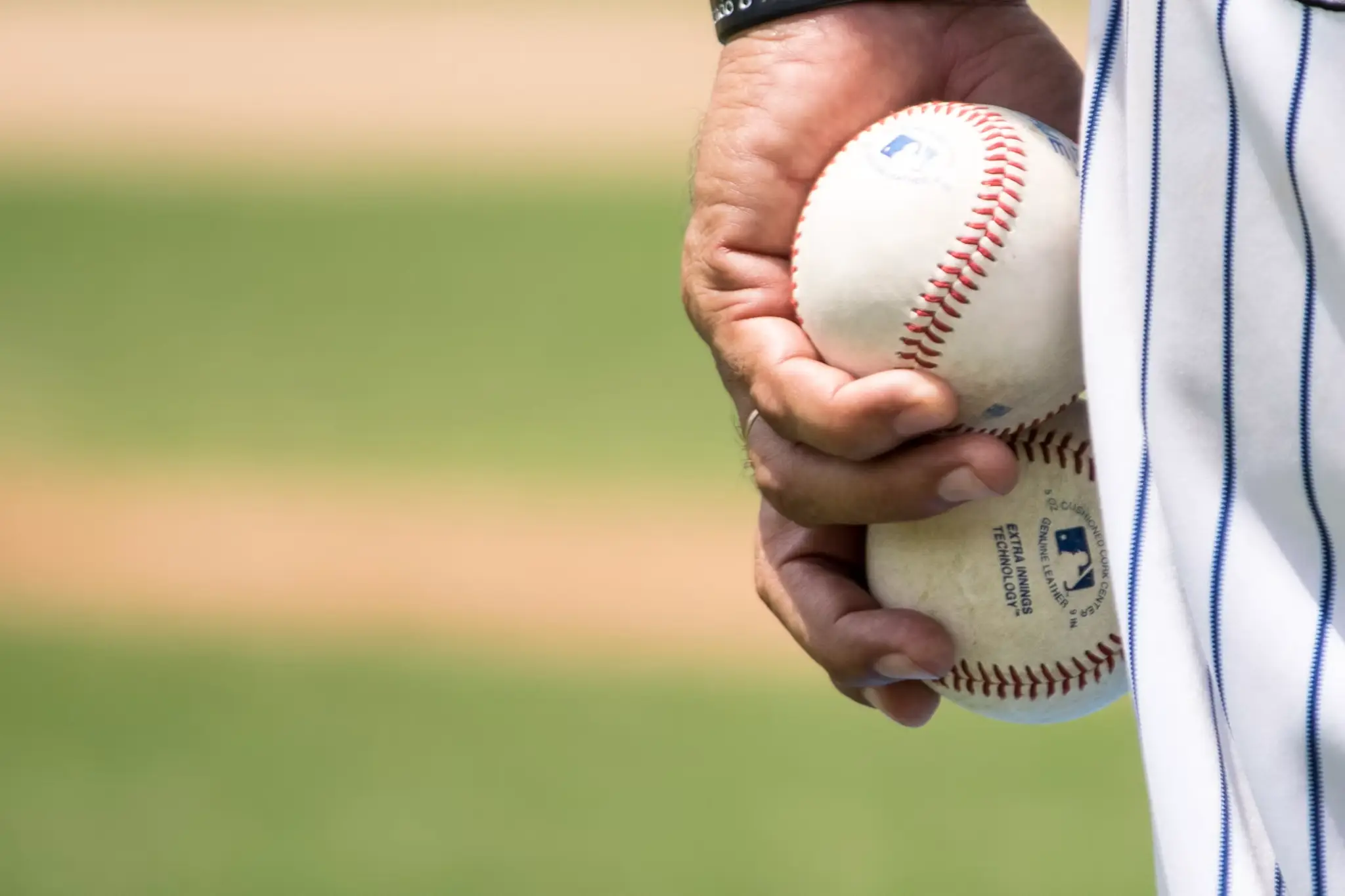 Hand holding two baseballs on a field with blurred grass background