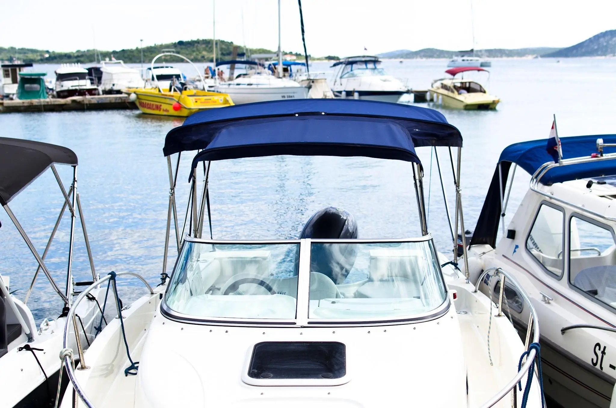 White speedboat with blue canopy docked in marina with other boats in background