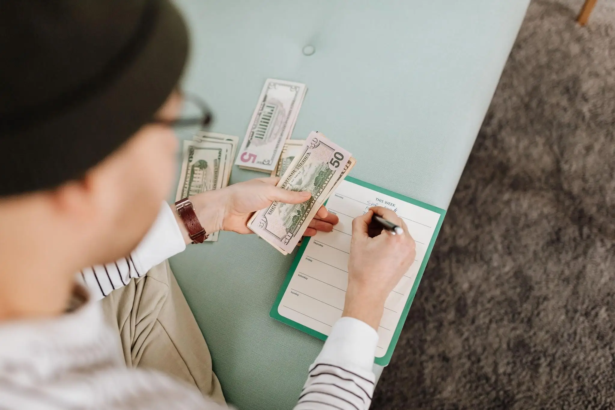 Person budgeting with cash and a planner on a light blue sofa