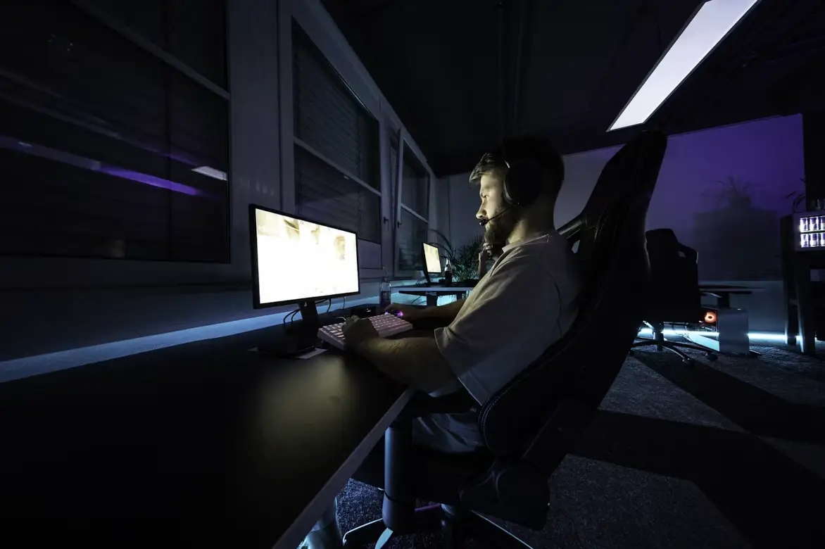 Man wearing headset gaming on computer in dark room with neon lighting