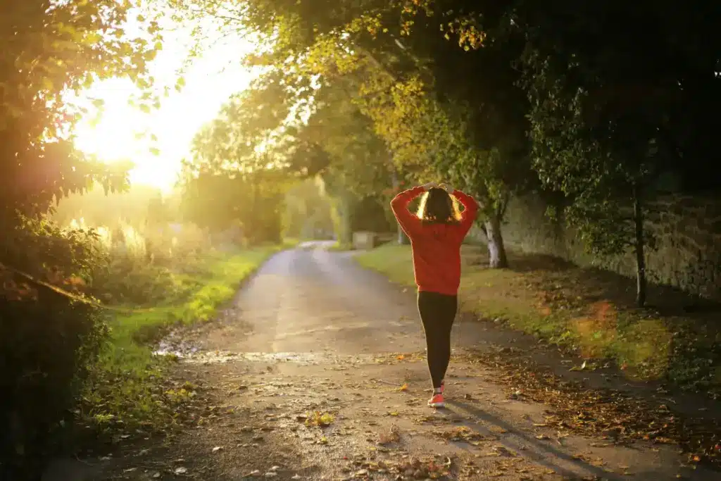Person in a red jacket walking on a sunlit path through trees