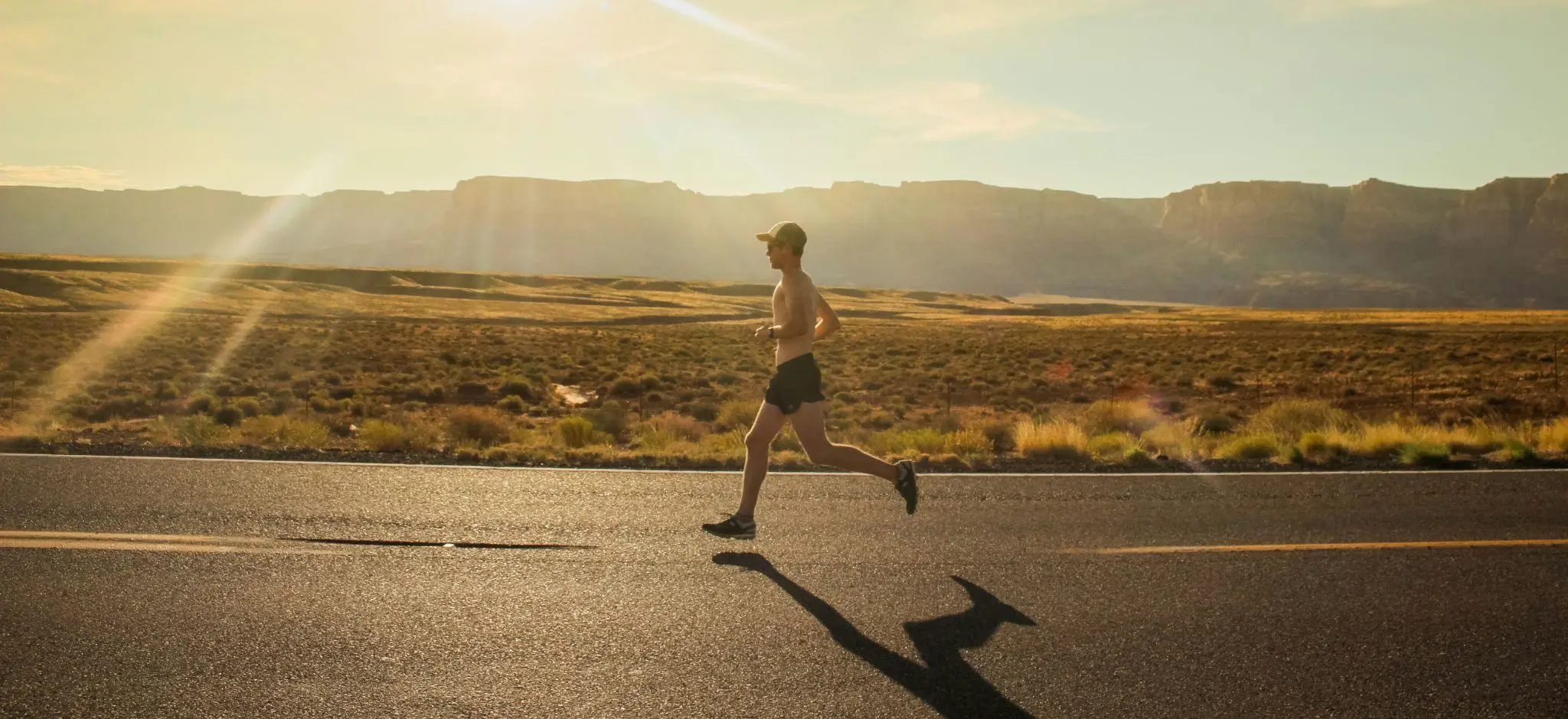 Man jogging on an empty road in a sunlit desert landscape