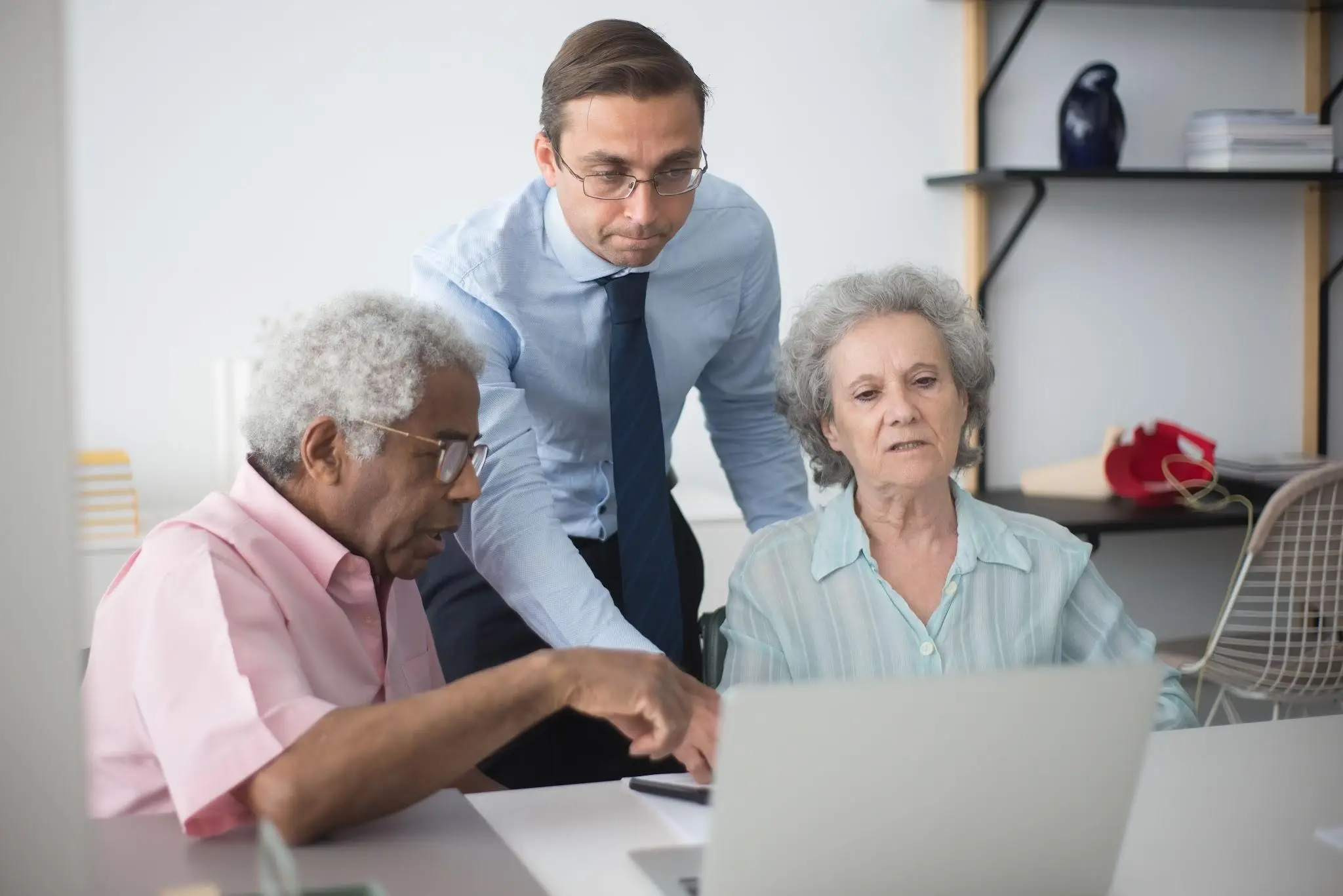 Man helping two older adults with laptop in a bright office setting