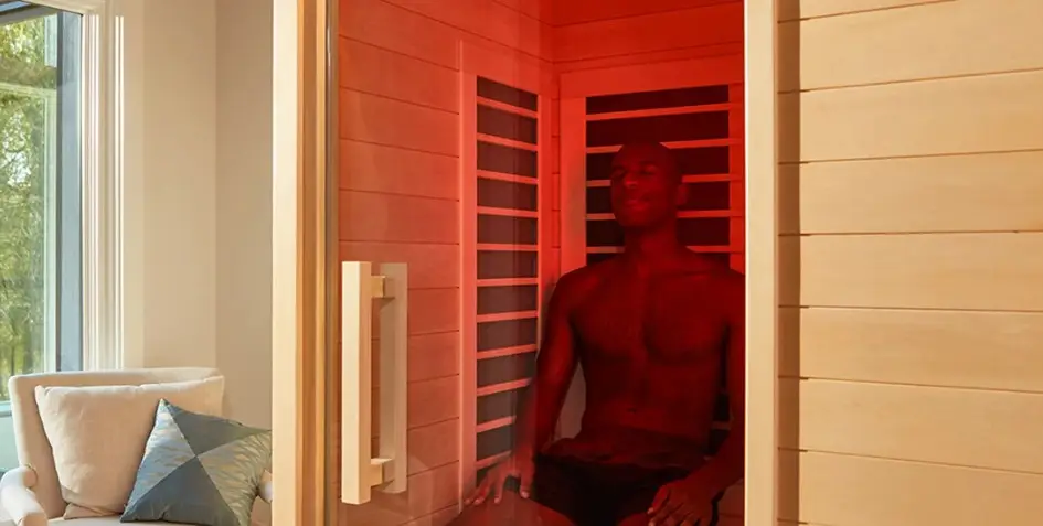Man sitting in infrared sauna with red lighting indoors near a window and sofa