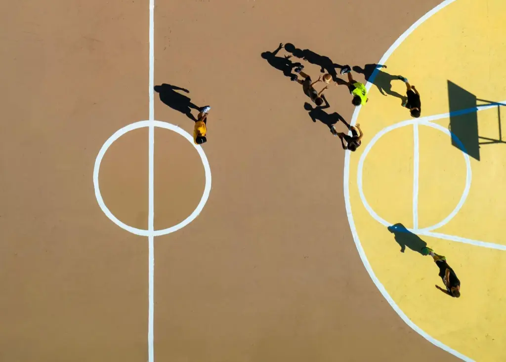 Basketball players in motion on outdoor court with distinct yellow and brown sections