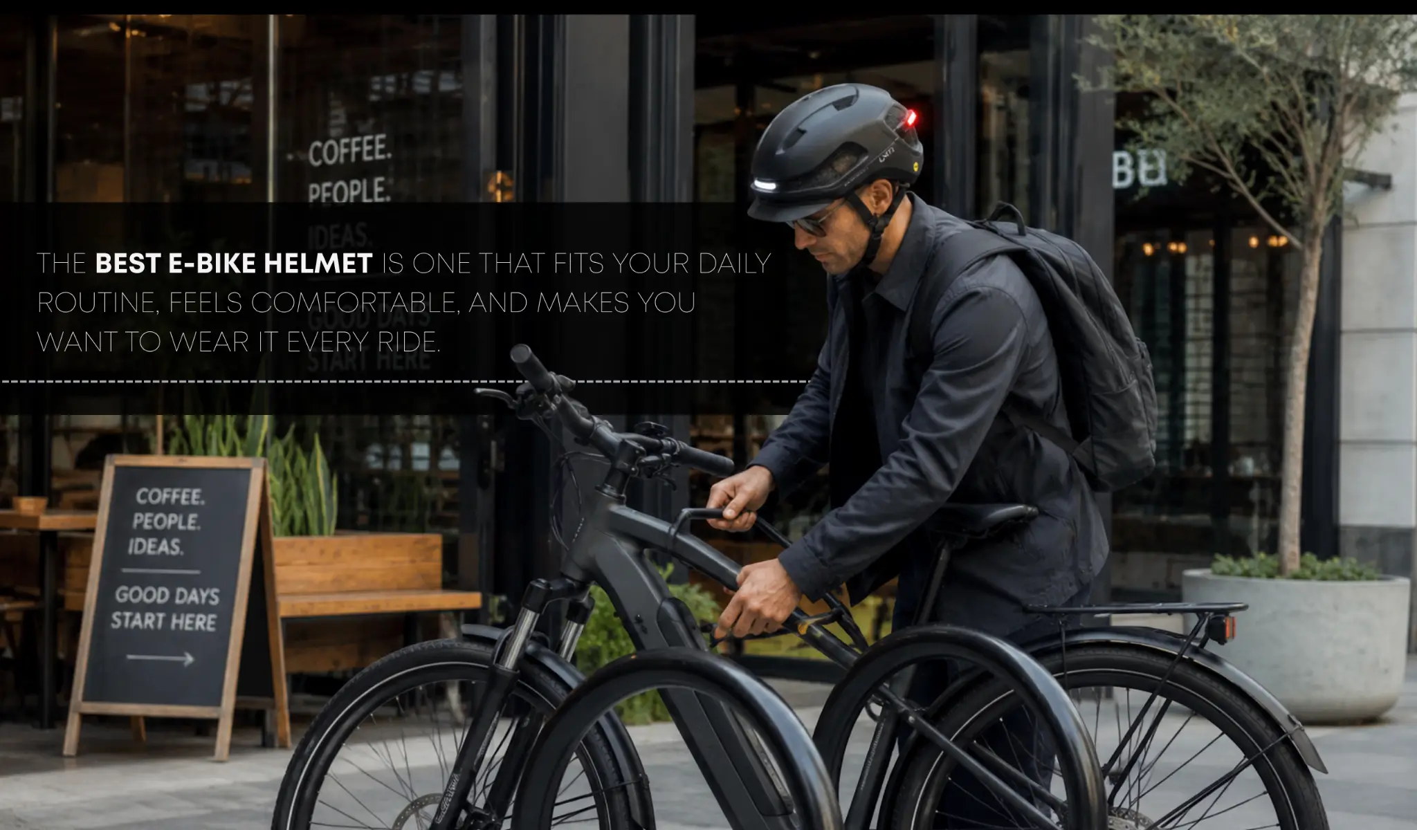 Man wearing e-bike helmet adjusting bicycle outside a café with wooden tables and greenery