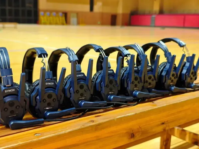Row of blue headsets with attached microphones on wooden table in a gymnasium