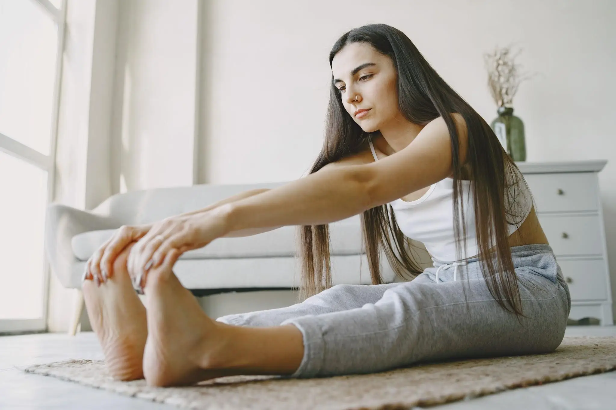 Woman doing seated forward bend exercise on a rug in bright living room environment