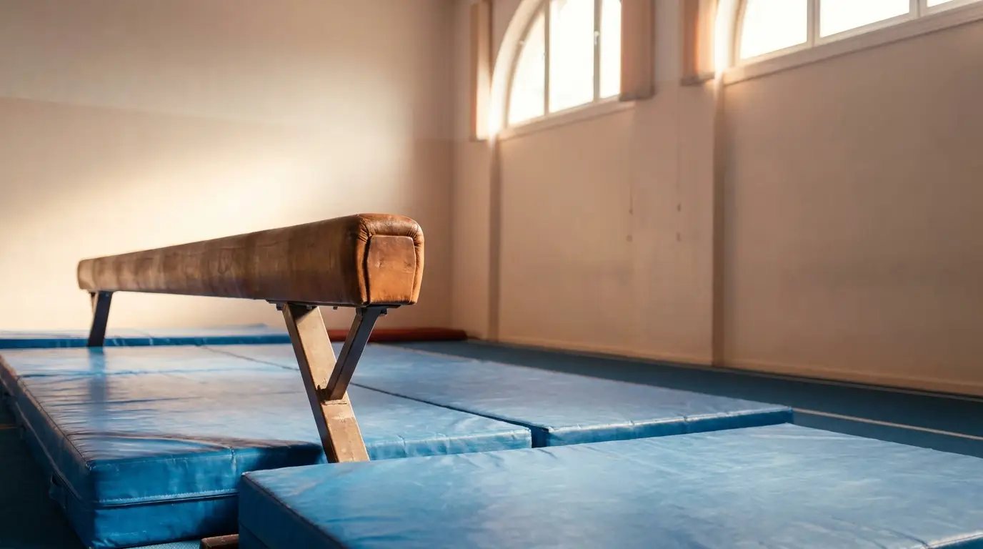 Gymnastic balance beam on blue mats in a sunlit gymnasium