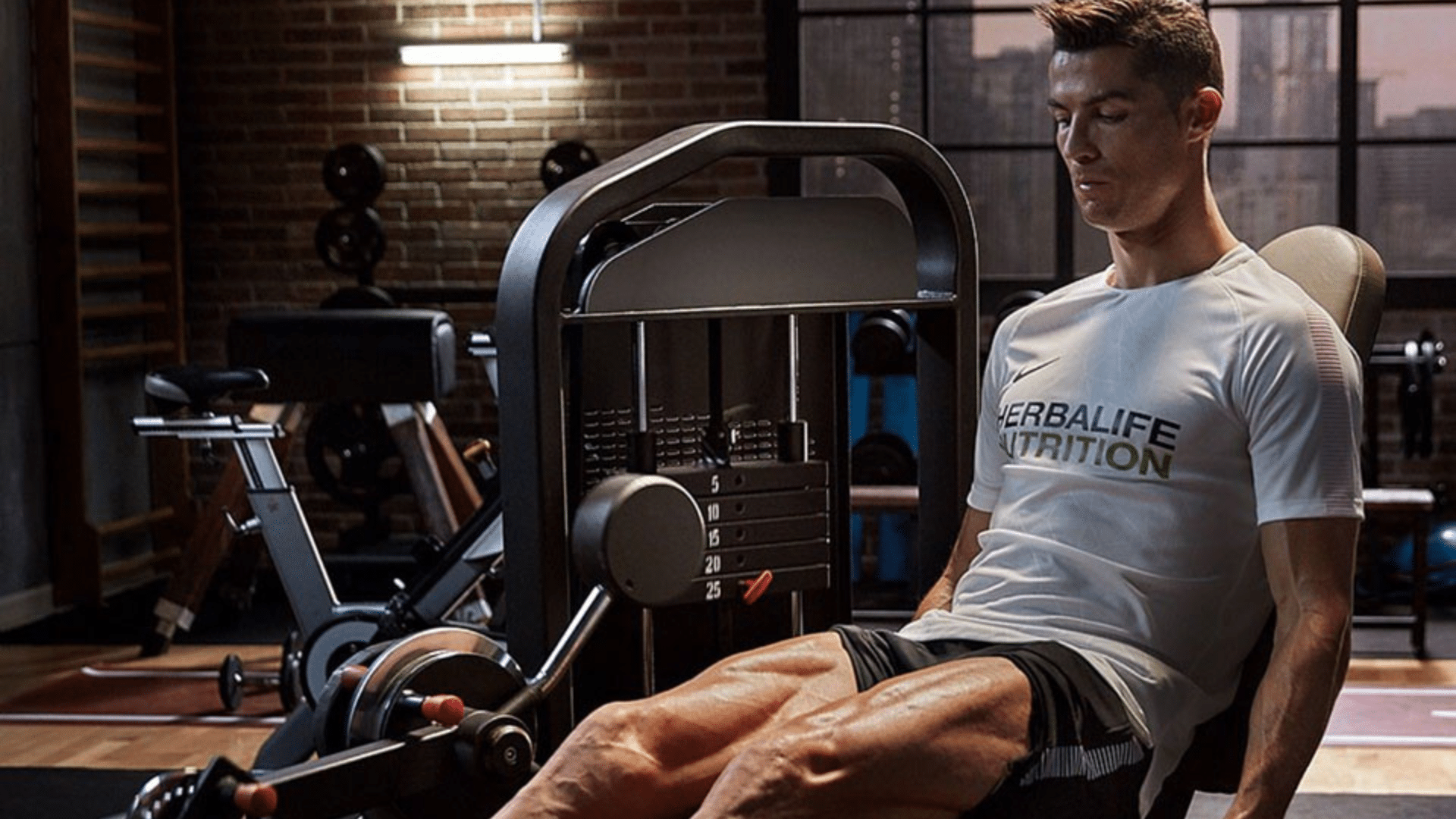 a football player using a leg extension machine during a focused strength workout in a modern gym wearing a white training shirt